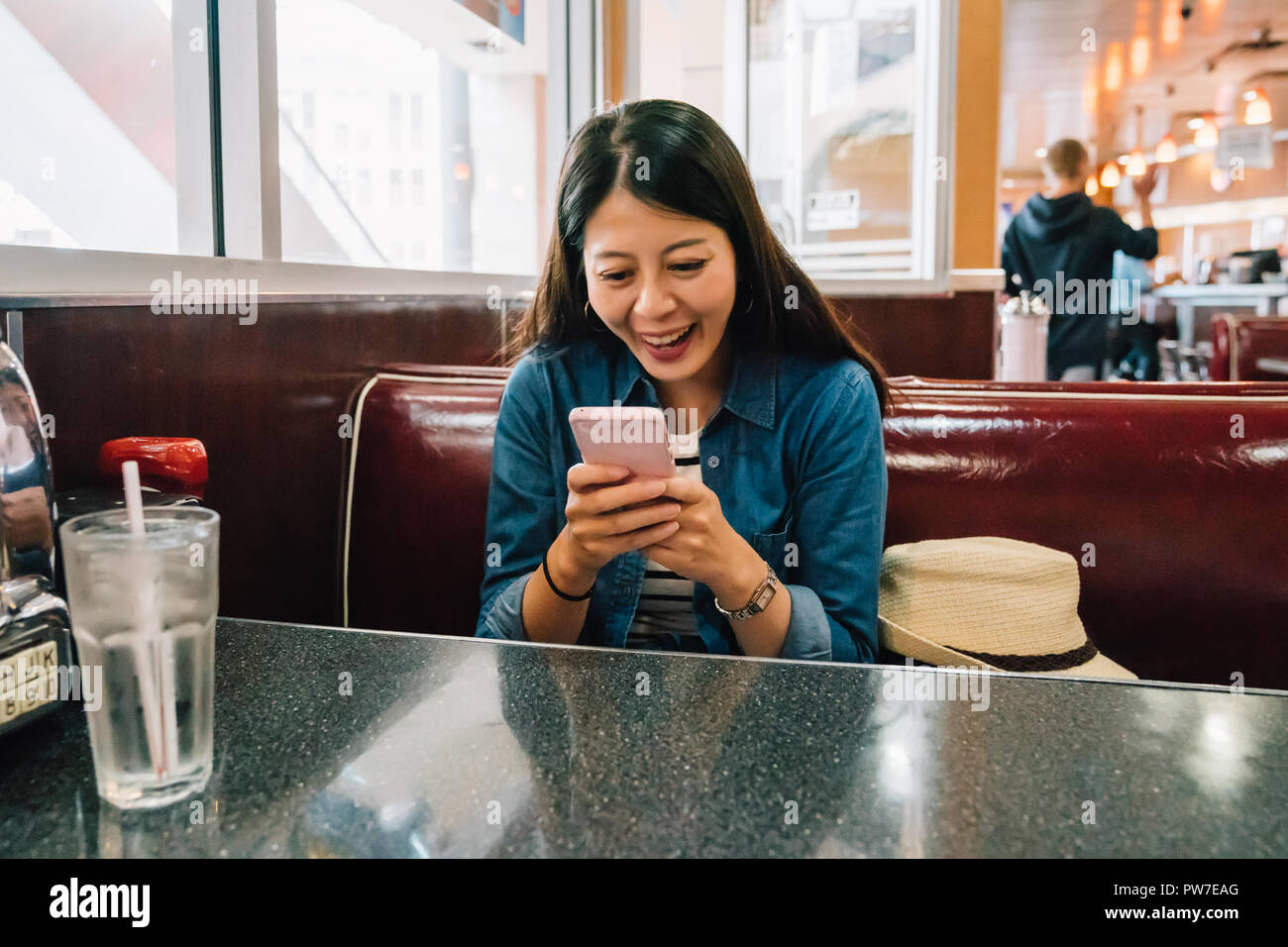 Lady casual relaxing assis dans la salle à manger et discuter joyeusement avec son amie en attendant le smartphone par repas. Jeune femme joyeusement en utilisant mobil Banque D'Images