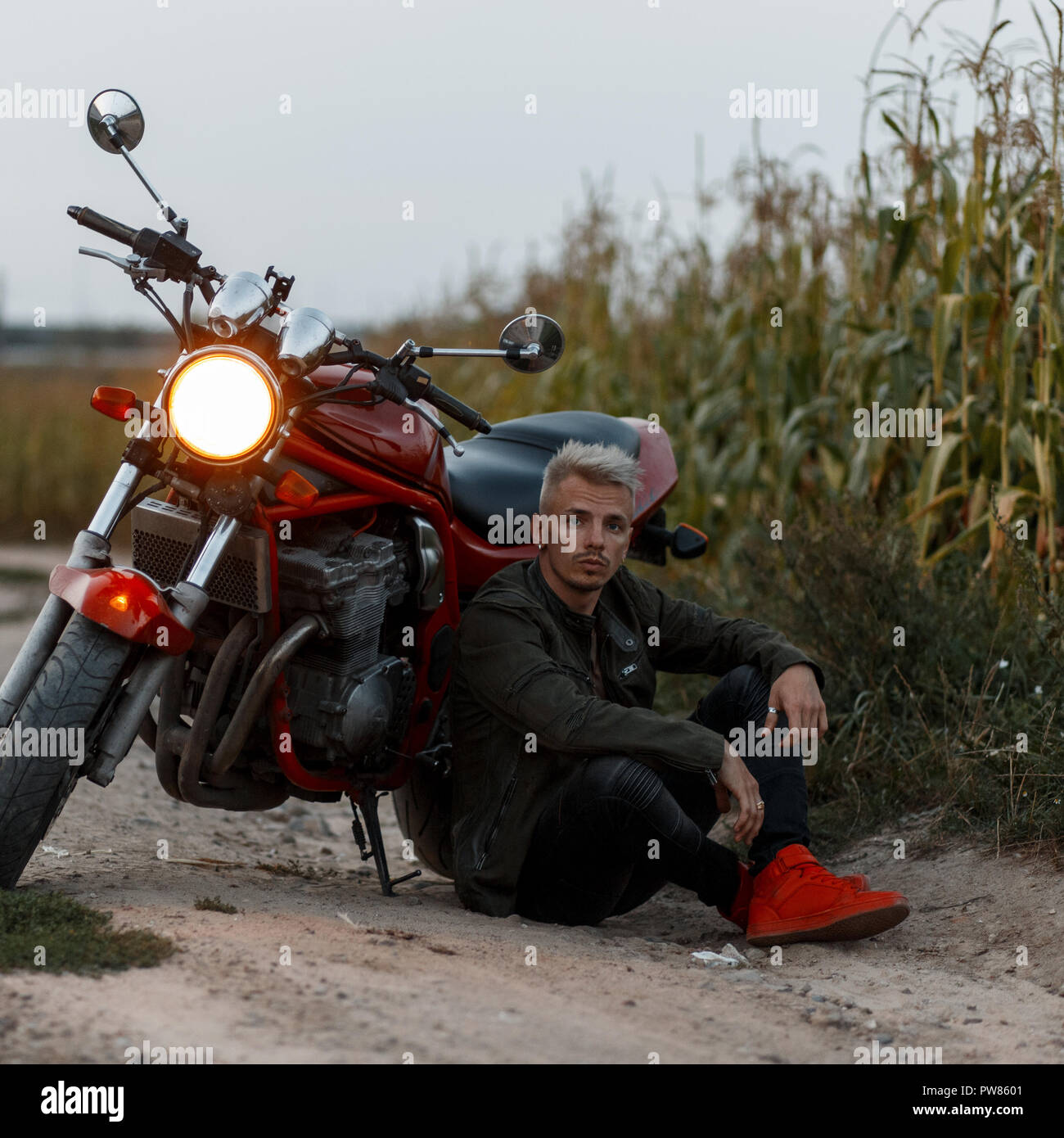 Beau à la mode homme brutal dans une veste kaki est assis près d'une moto  dans le domaine Photo Stock - Alamy