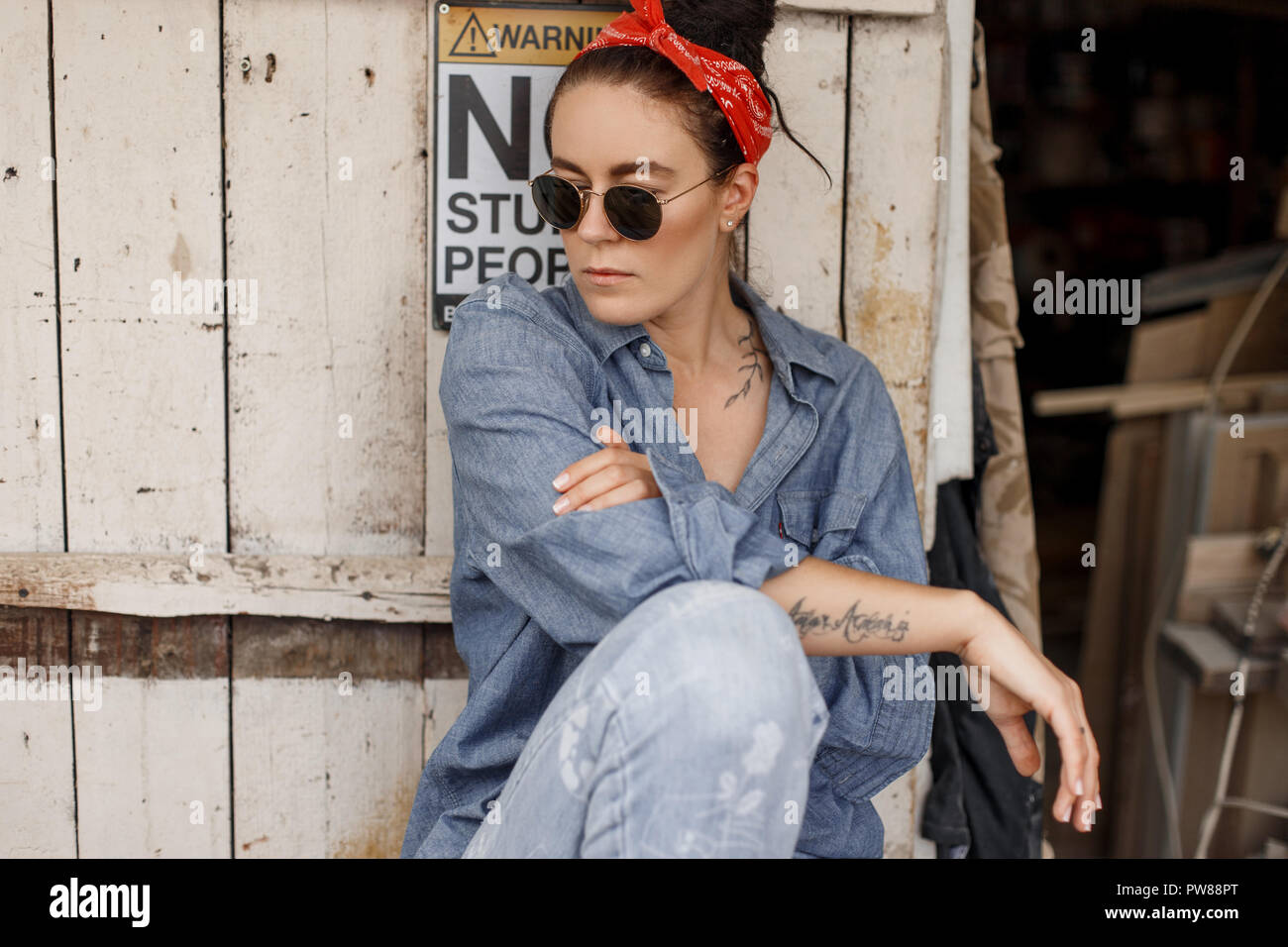 Hipster femme en denim jeans avec des vêtements à la mode avec un bandana  rouge et des lunettes de soleil est assis près d'un bois en bois vintage  Photo Stock - Alamy