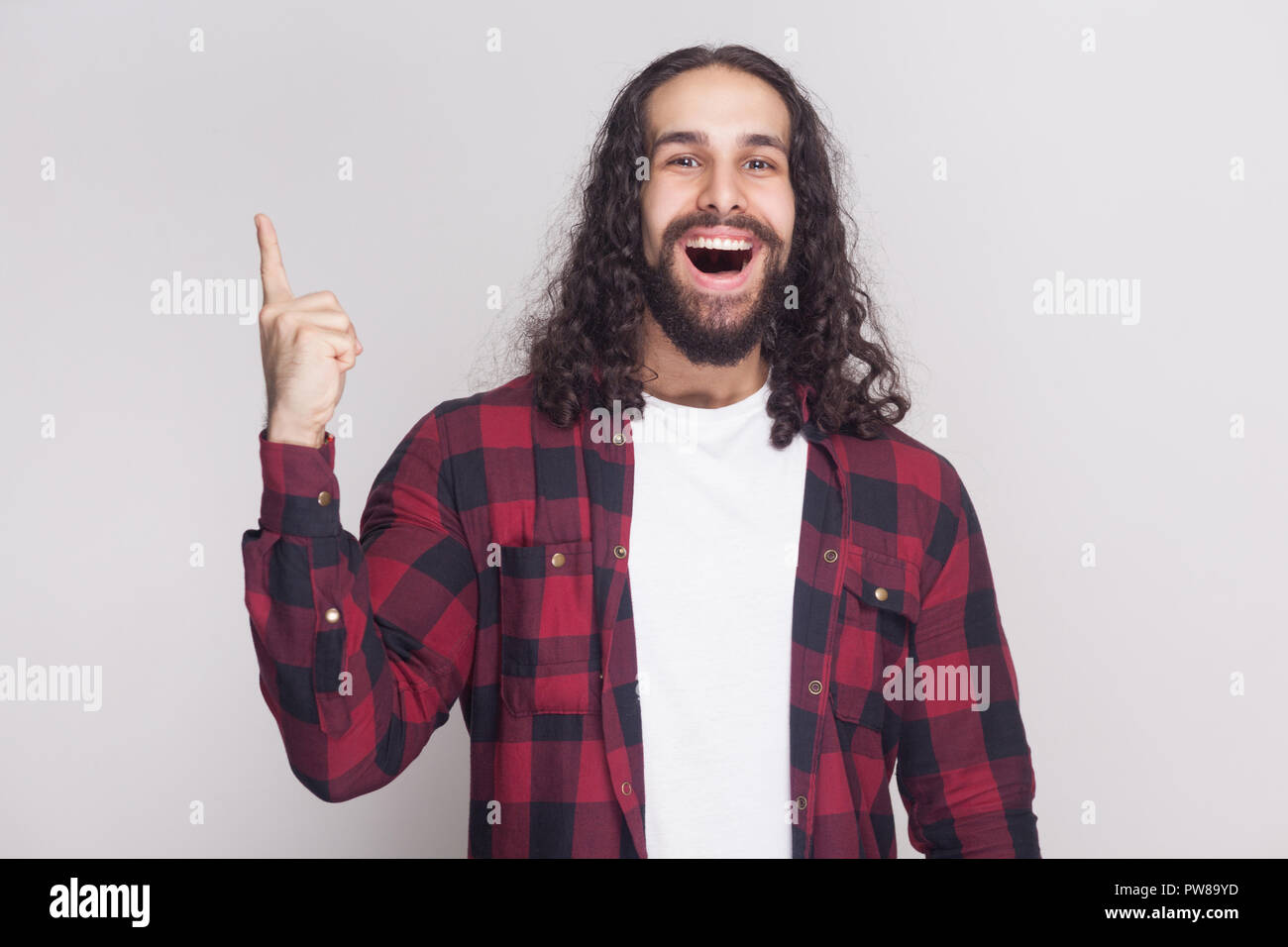 J'ai une idée. Heureux surpris bel homme avec barbe et black long cheveux bouclés en chemise rouge à carreaux occasionnel, permanent à la caméra au doigt avec u Banque D'Images