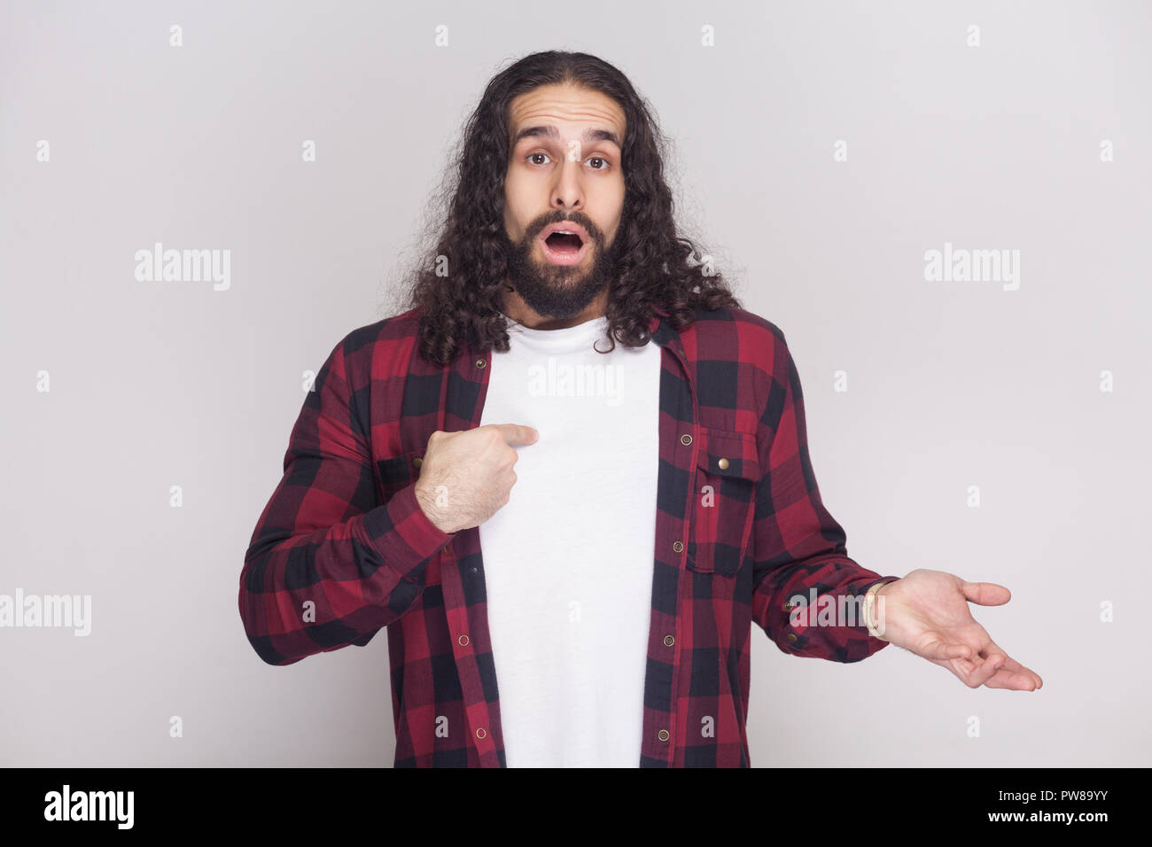 Est-ce moi ? ! Surpris bel homme avec barbe et black long cheveux bouclés en chemise rouge à carreaux décontractée standing looking at camera et vers lui-même. Banque D'Images Est-ce moi ? ! Surpris bel homme avec barbe et black long cheveux bouclés en chemise rouge à carreaux décontractée standing looking at camera et vers lui-même. Banque D'Images