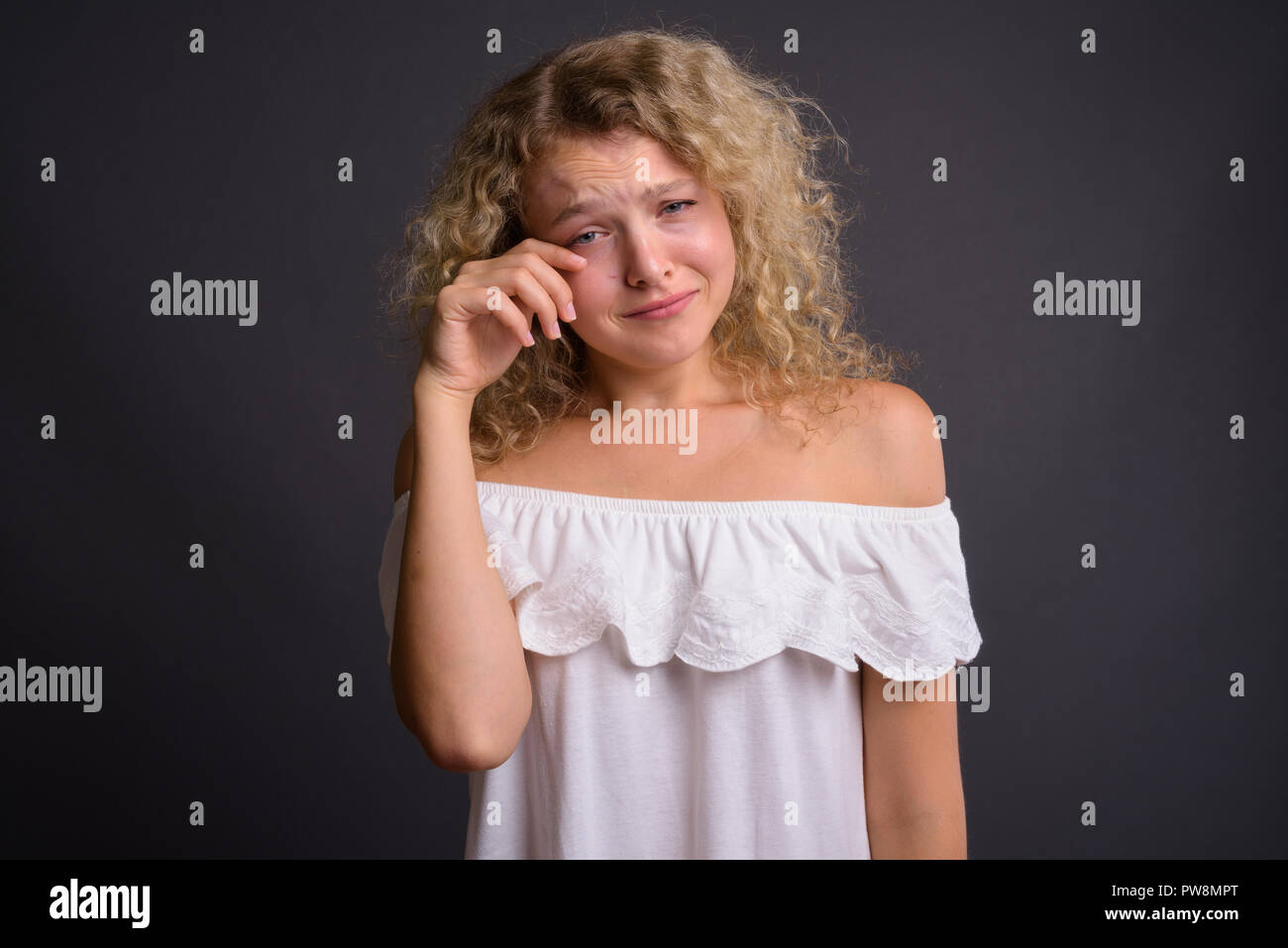 Belle jeune femme aux cheveux bouclés blonds contre gray background Banque D'Images