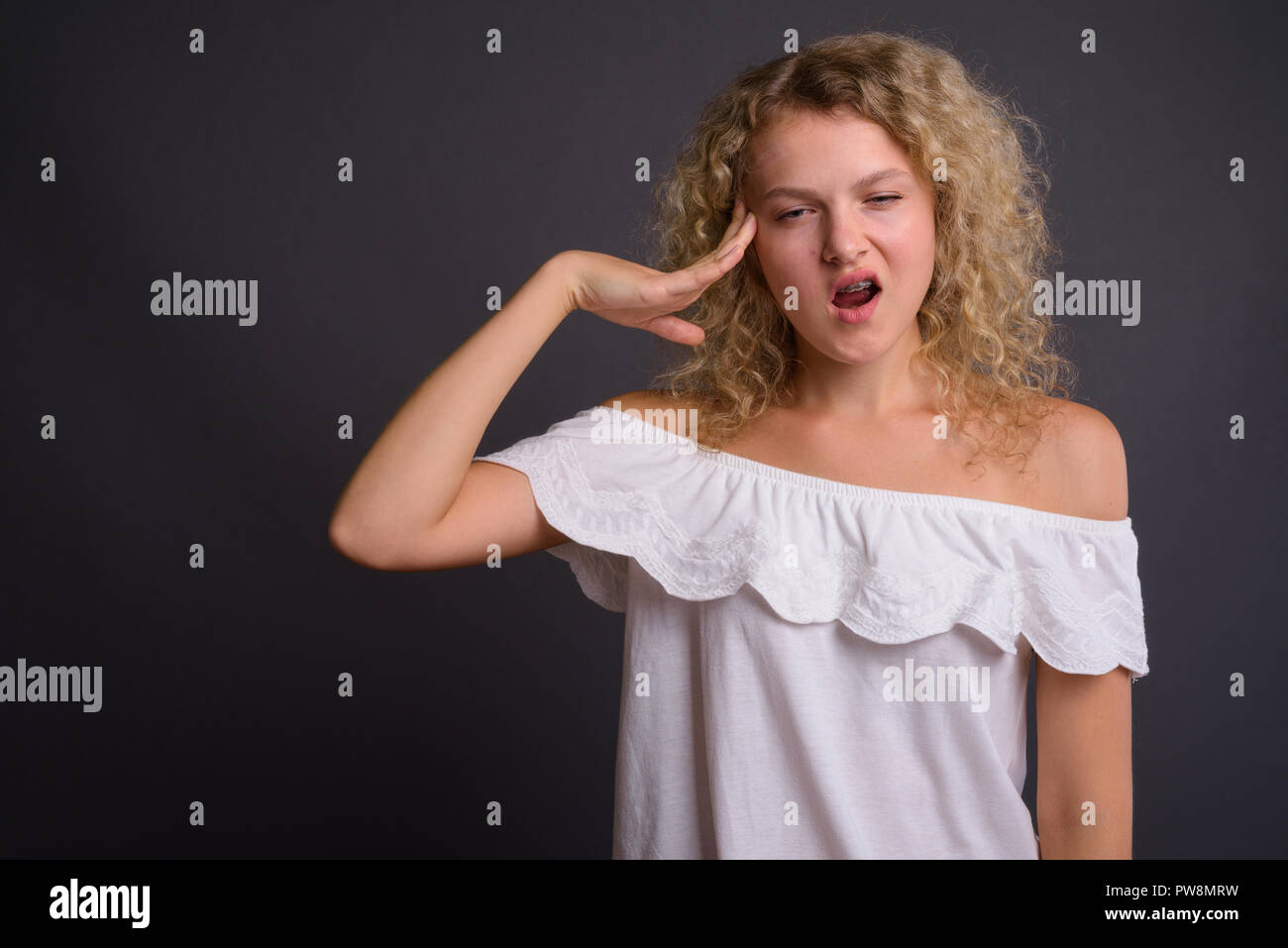 Belle jeune femme aux cheveux bouclés blonds contre gray background Banque D'Images