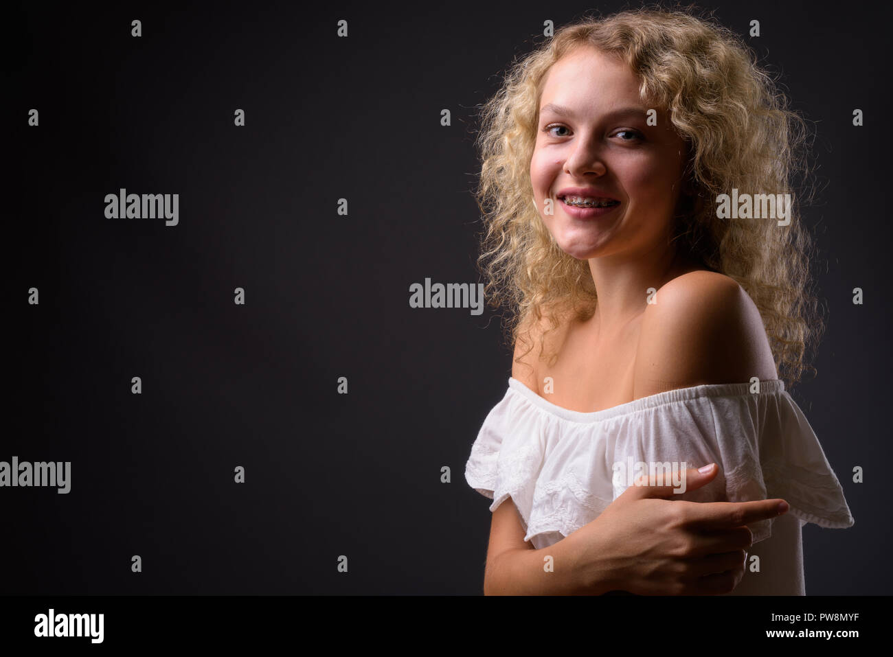 Belle jeune femme aux cheveux bouclés blonds contre gray background Banque D'Images