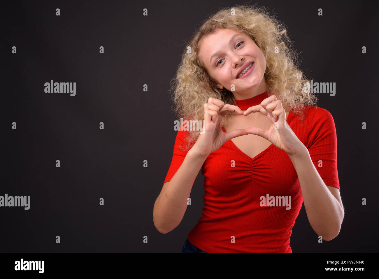 Belle jeune femme aux cheveux bouclés blonds contre gray background Banque D'Images