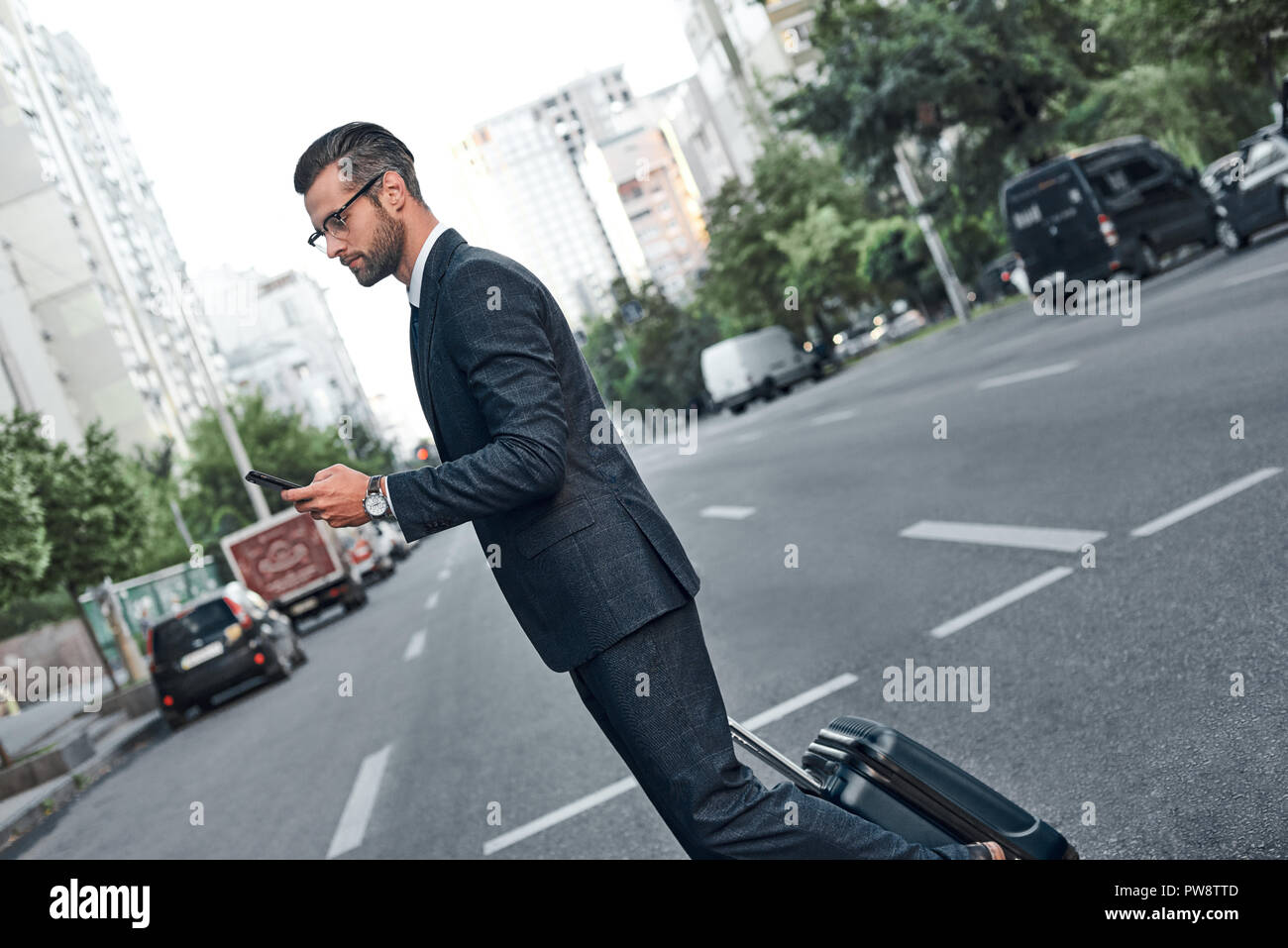 Un jeune homme avec glases est chatter sur son smartphone et traverse la route Banque D'Images