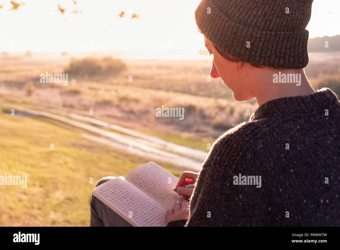 Écrire un journal intime dans une nature magnifique. Woman facing soir soleil prend des notes sur un bloc-notes Banque D'Images