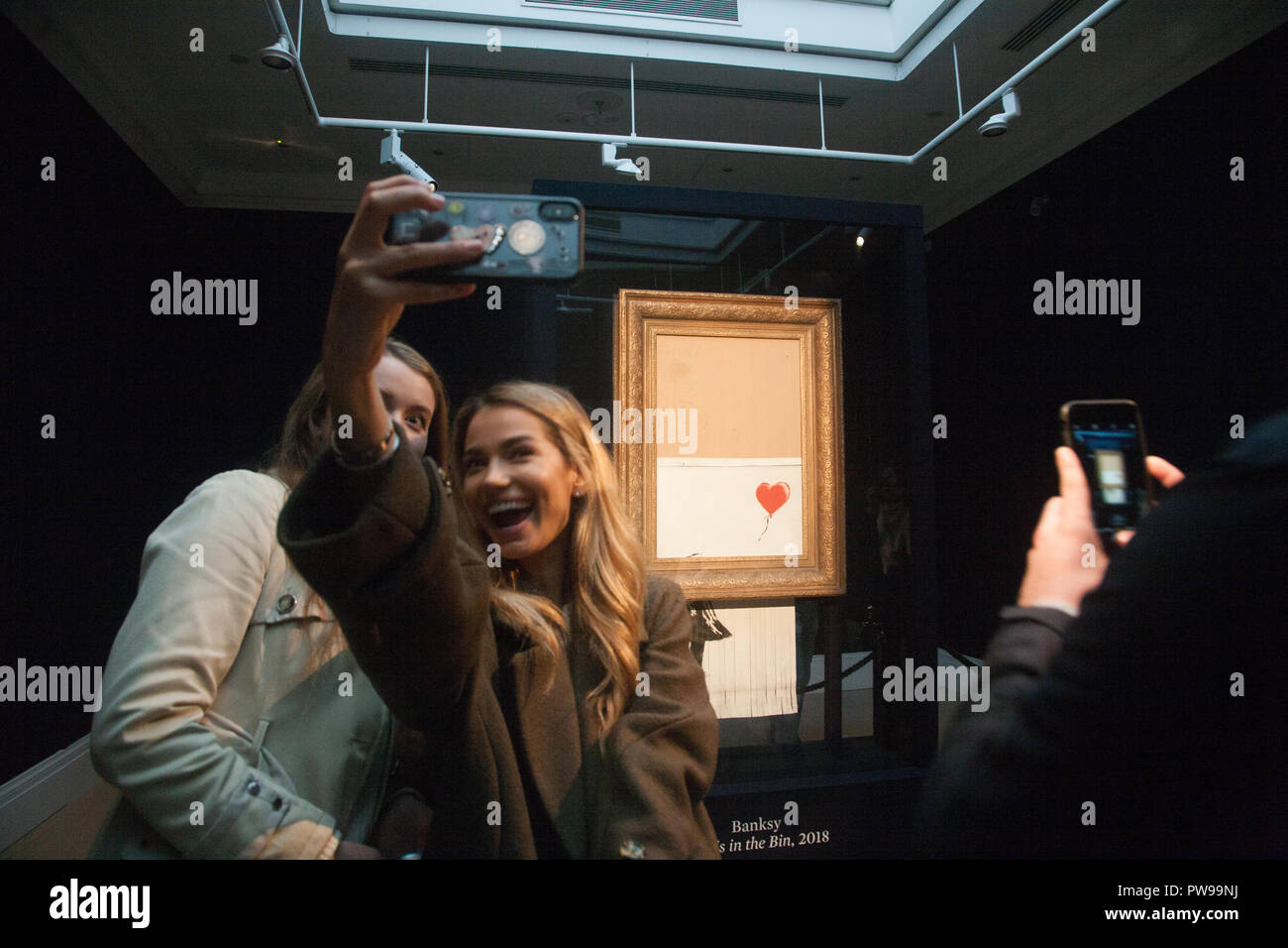 London UK. 14 octobre 2018. Visiteurs les autoportraits en face de Banksy's 'Amour dans le bin' qui est sur avis au public à Sothebys à New Bond Street à Londres. L'œuvre qui était anciennement connu sous le nom de 'La petite fille avec un ballon" a été déchiquetés quelques instants après la soumission gagnante et le marteau est tombé à l'enchère à un acheteur étranger le 5 octobre : Crédit amer ghazzal/Alamy Live News Crédit : amer ghazzal/Alamy Live News Banque D'Images