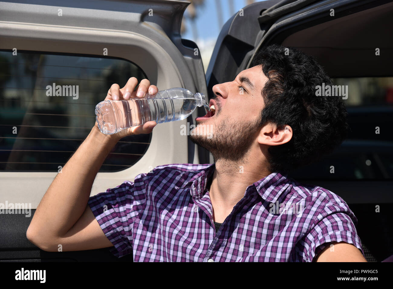 Beau jeune homme, verser de l'eau dans sa bouche sur la porte arrière de sa voiture Banque D'Images