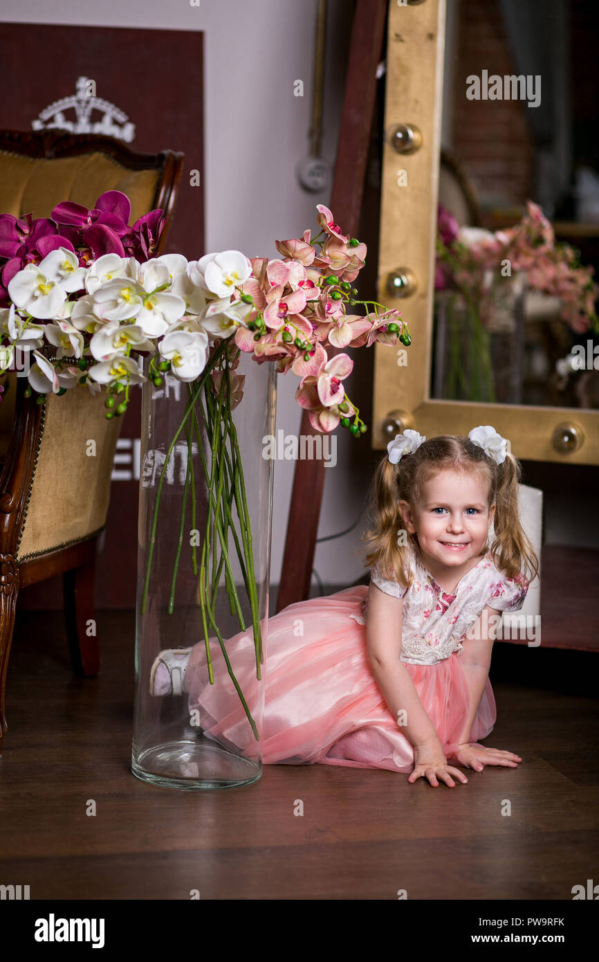 Blue-eyed jolie fille dans une robe rose assis près d'un vase d'orchidées et souriant Banque D'Images