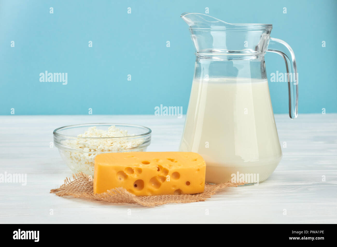 Produits laitiers sur fond bleu. Verseuse en verre dans le lait, le fromage cottage et le fromage Maasdam. Lait délicieux aliments. Banque D'Images