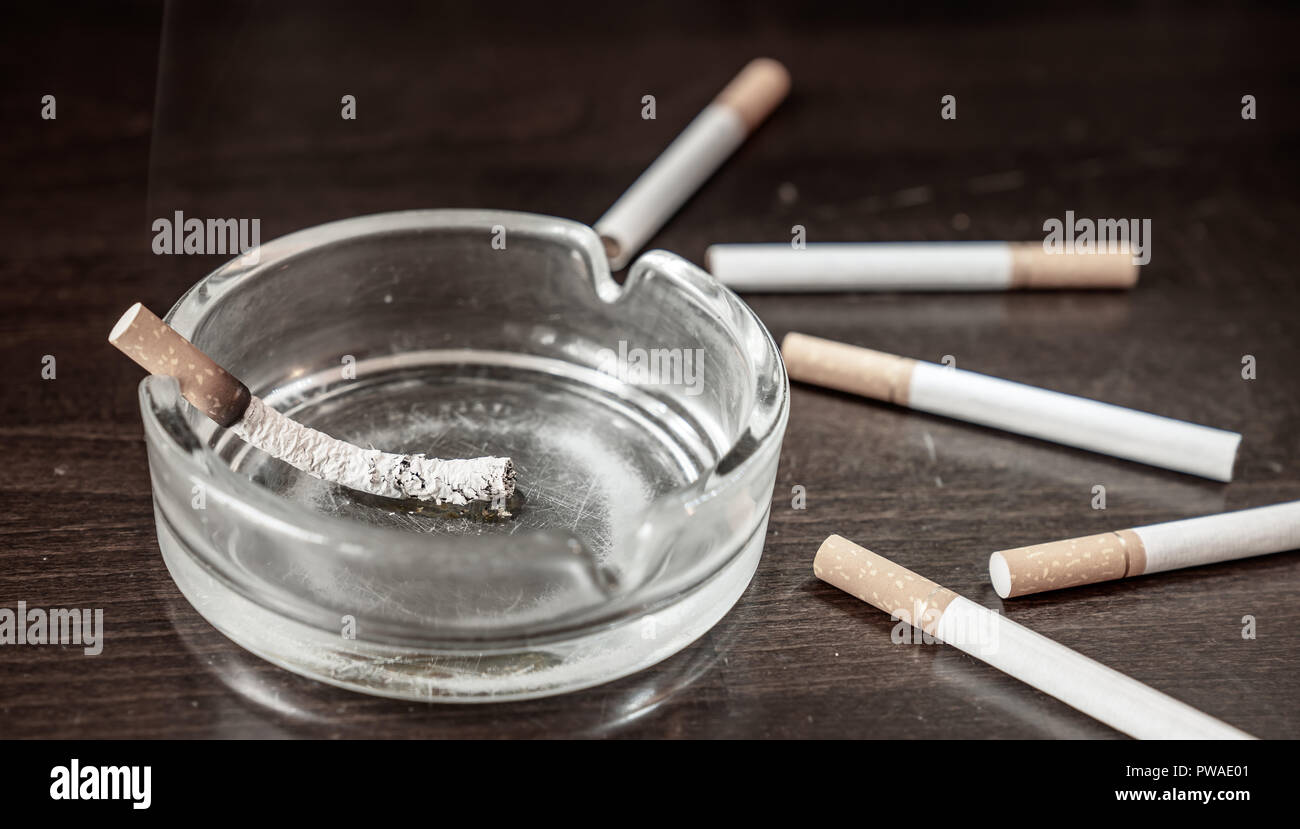 Un scintillant des brûlures de cigarette dans un cendrier sur une table avec des cigarettes autour d'elle Banque D'Images