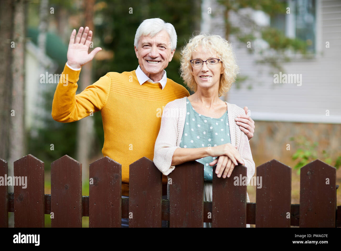 Hospitalier mature couple standing by fence tout en agitant la main de l'homme sympathique à leurs voisins Banque D'Images