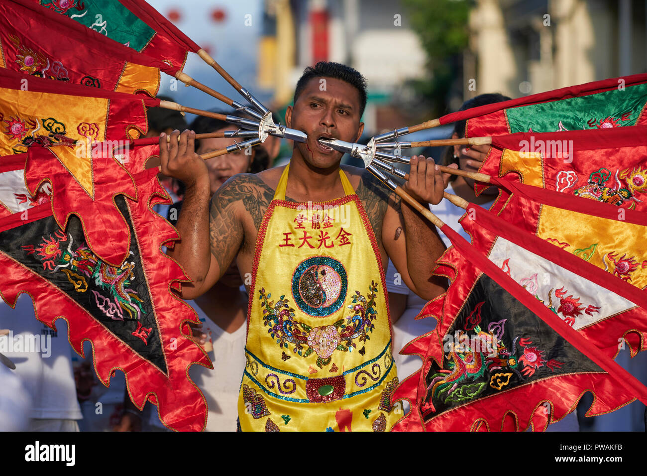 Lors du Festival végétarien de Phuket Town, en Thaïlande, un homme affiche des joues percées de poignées de drapeaux portant ainsi une multitude de drapeaux religieux Banque D'Images