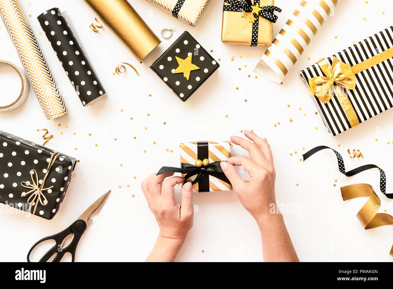 Vue de dessus de mains femelle rétractable des boîtes-cadeaux, dispersés dans divers matériaux d'emballage noir, blanc et doré. Un concept de Noël, Nouvel An Banque D'Images