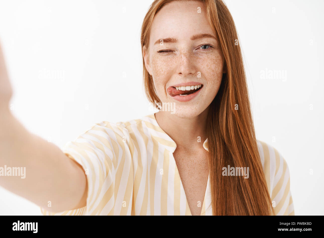 Belle femme rousse féminin avec mignon rousseur clignant de sticking out tongue flirty et joyeusement la main en tirant vers la caméra comme si la prise sur smartphone selfies tout en étant en vacances Banque D'Images