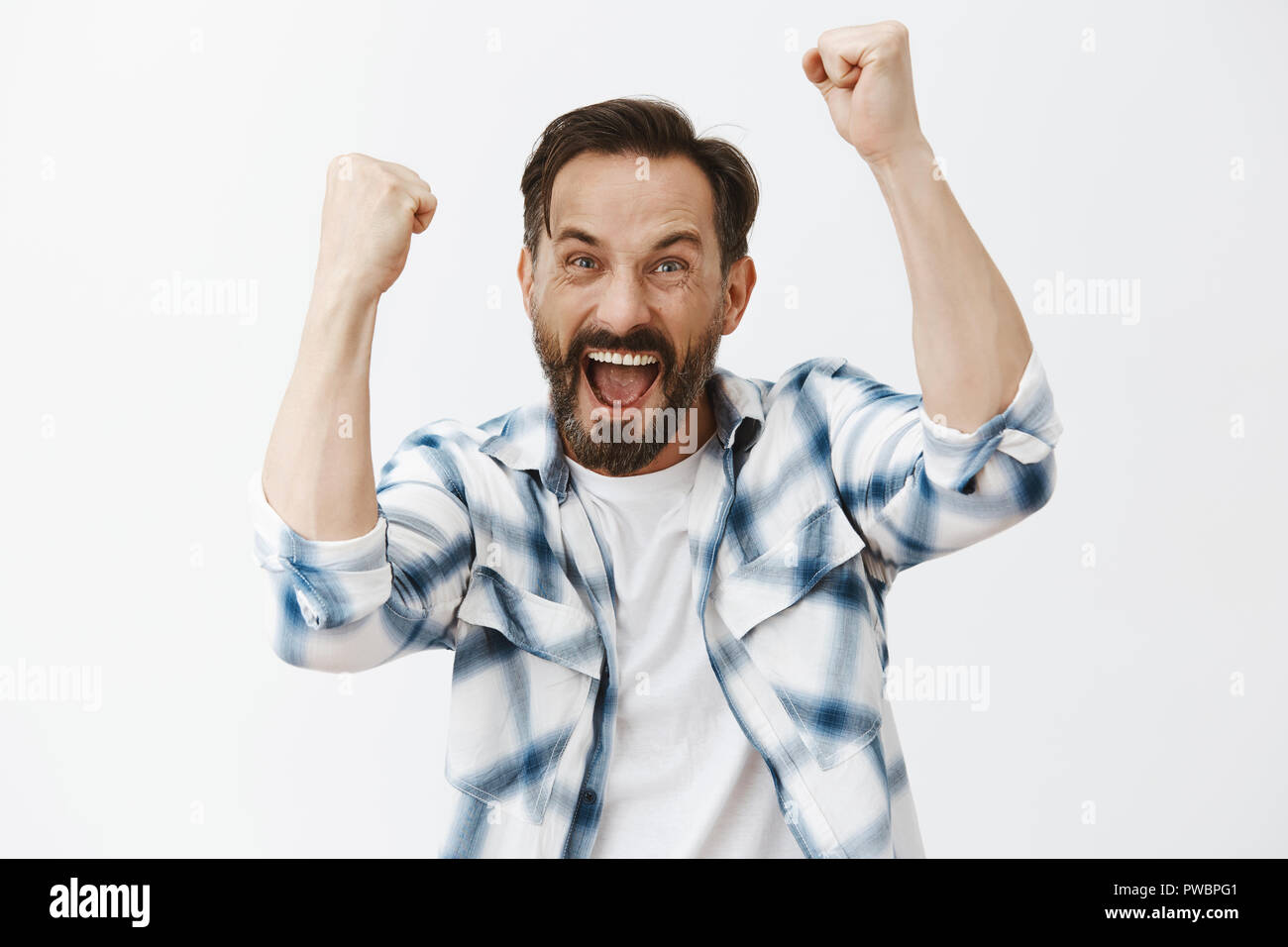 Ouais Allez on va gagner. Portrait of happy joyeux et maturité émotive guy européenne avec barbe et cheveux noirs, soulevant des poings et crient, triomphant ou acclamer tout en regardant match de football dans un pub Banque D'Images