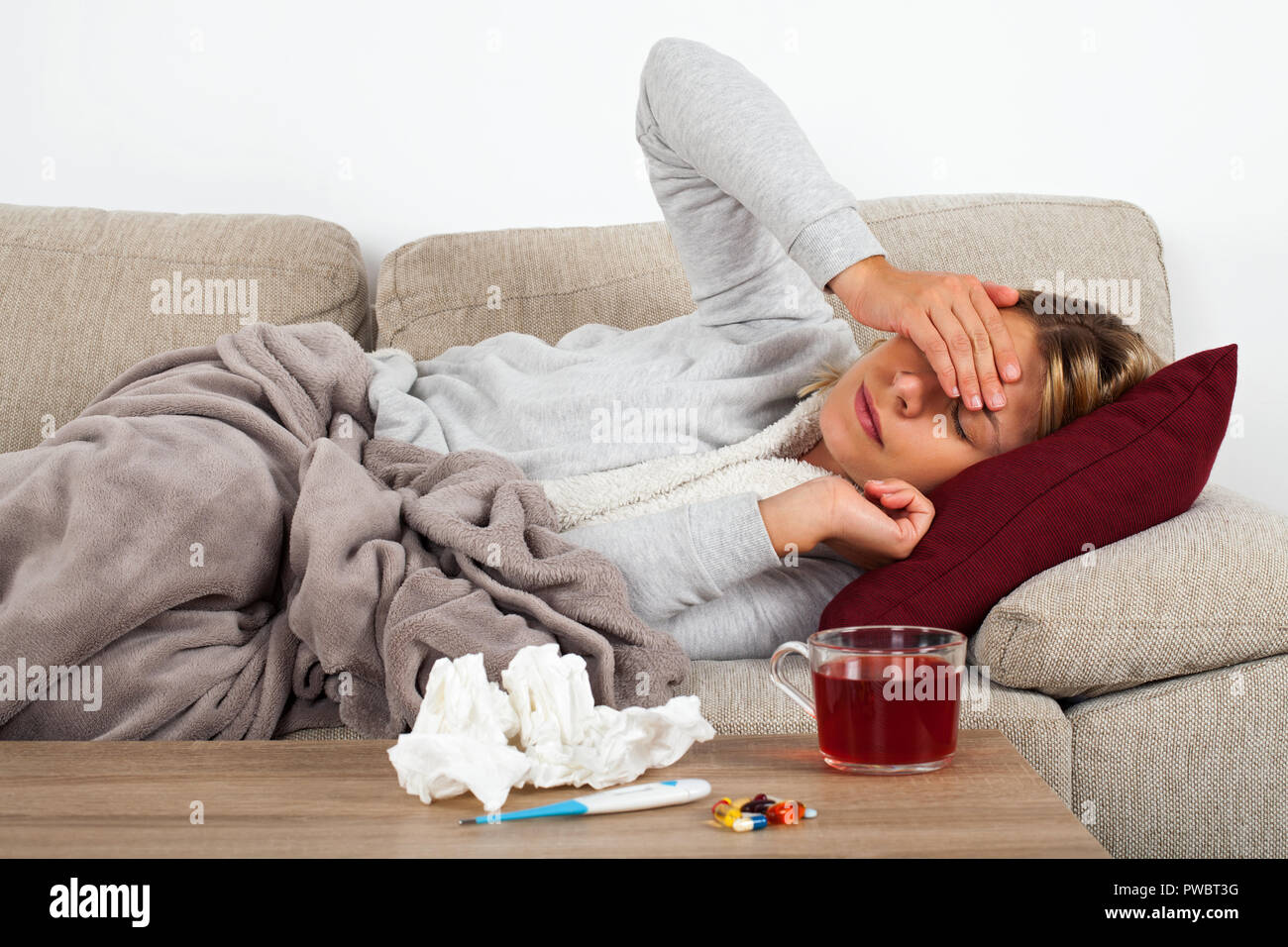 Femme malade allongé sur le canapé enveloppé dans une couverture chaude -  médicaments, thermomètre et d'un plateau sur la table Photo Stock - Alamy