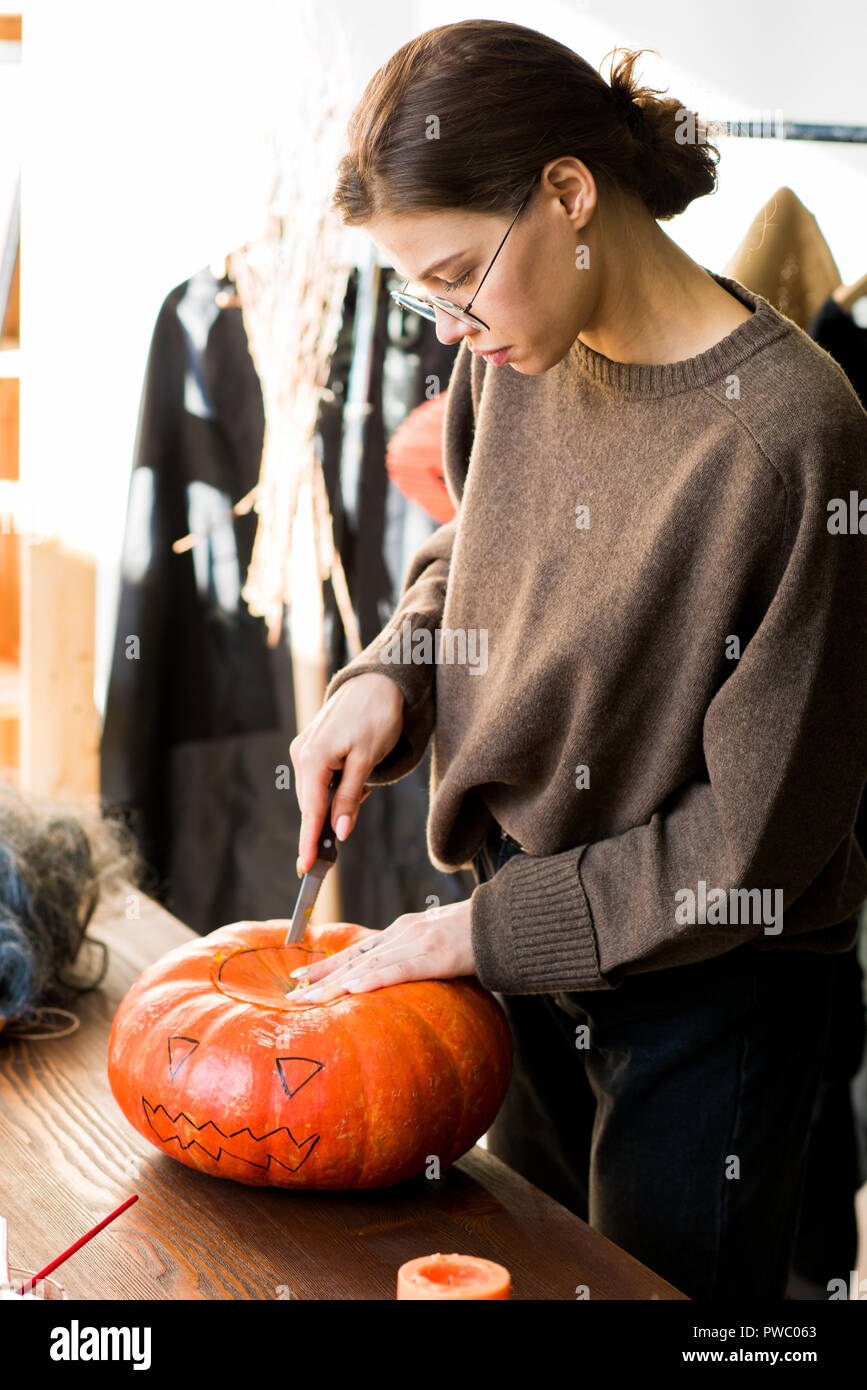 Les jeunes qualifiés confiance sérieux artisane dans les verres debout à table en bois et couvercle en citrouille coupe l'alimentation de la sculpture pour l'Halloween en design stu Banque D'Images