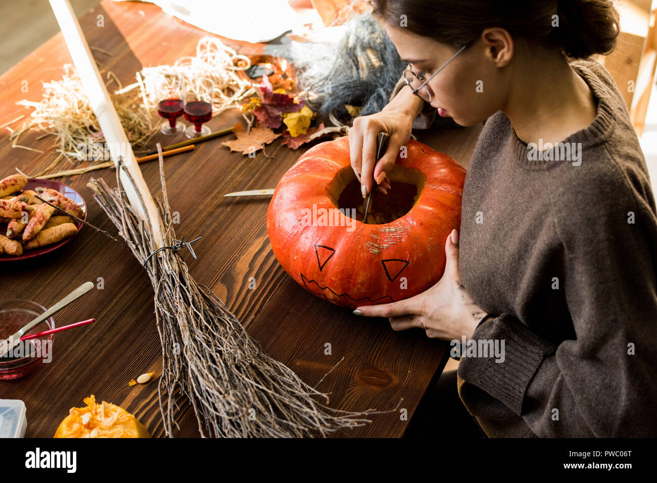 Jeune femme sérieuse concentrées dans les verres assis à table avec plein de trucs et d'enlever les graines de citrouille tout en se préparant pour la sculpture en atelier Banque D'Images