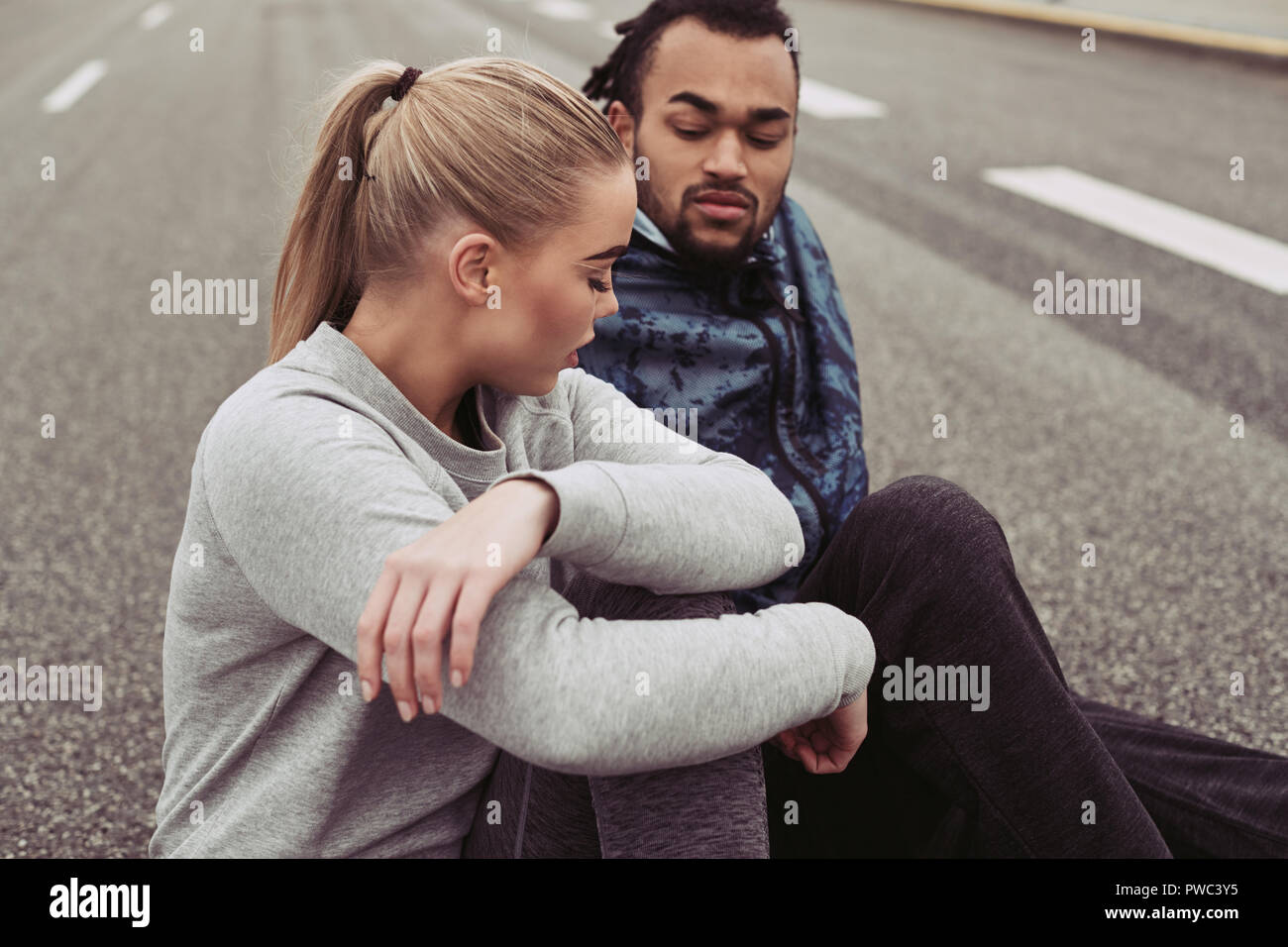 Jeune couple divers dans les vêtements de sport assis ensemble sur une route et prendre leur souffle tandis que dehors pour un jogging Banque D'Images