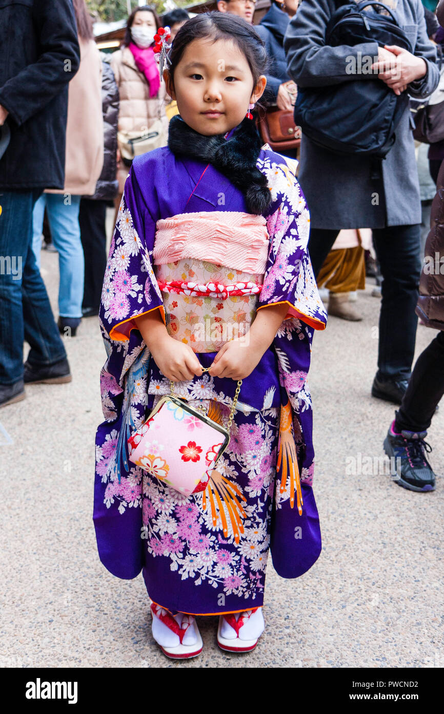 Nouvel An japonais, shogatsu. Petite fille, enfant, 5-6 ans, l'article de poser portant des Kimono mauve, et la tenue de petit sac à main. Contact avec les yeux. Banque D'Images