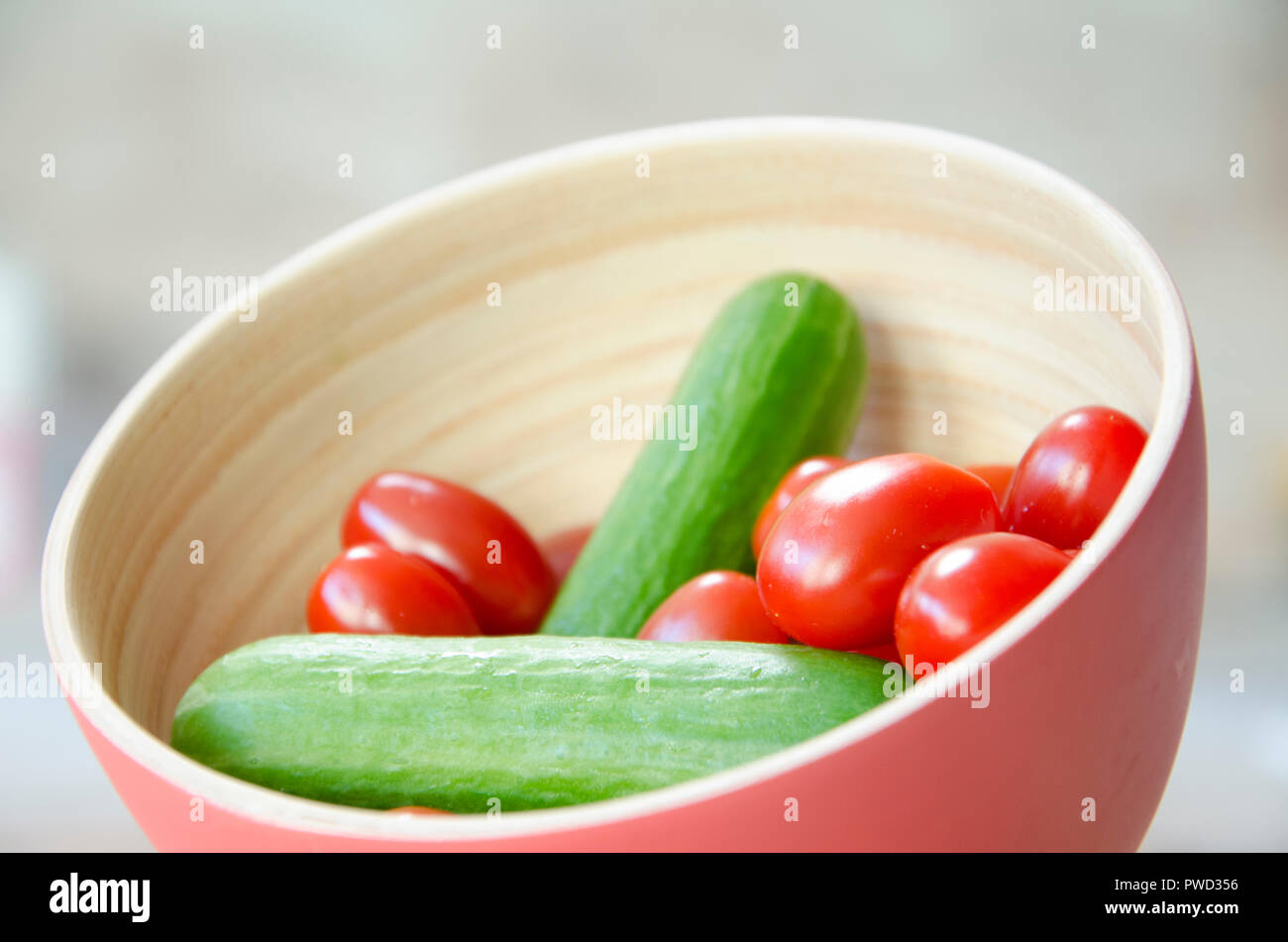 Mini tomates avec mini concombres dans un bol en bois. Couleurs douces, parfait pour un restaurant ou dîner. Les légumes dans un bol, des aliments santé. Banque D'Images