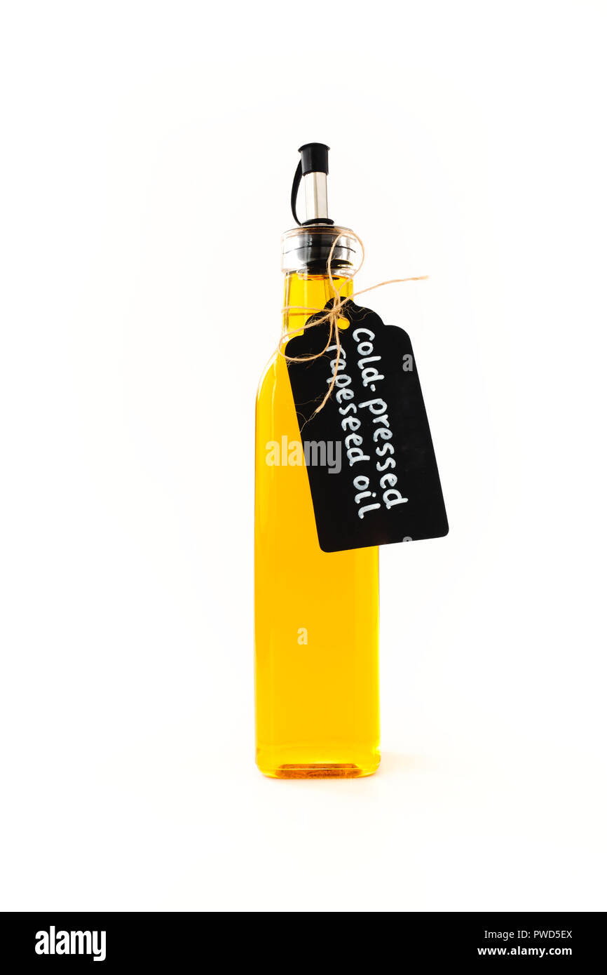 L'huile de colza dans un grand flacon en verre rectangulaire avec bec verseur en acier inoxydable, ornée d'une étiquette de papier noir et de jute bow, isolé sur blanc retour Banque D'Images