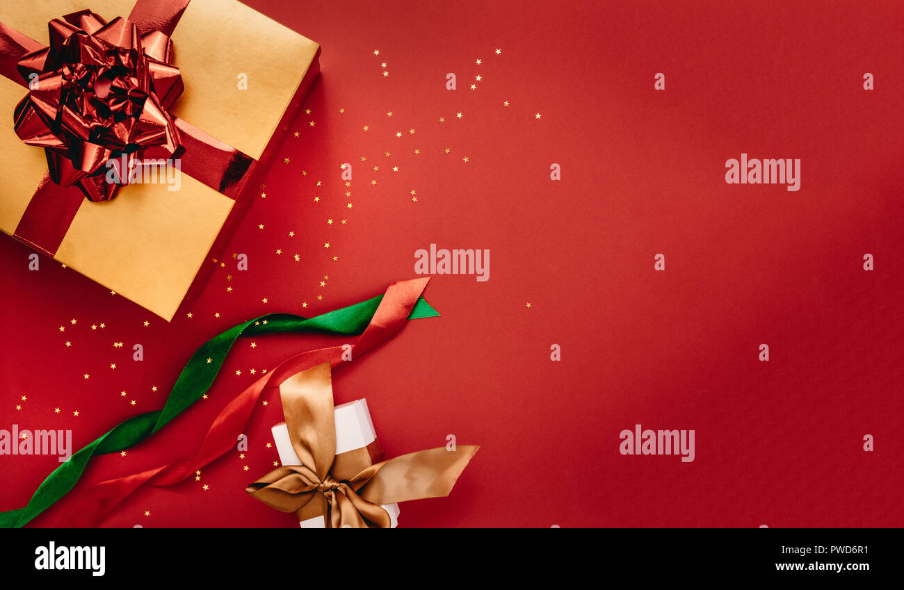 Présenter des boîtes et étoiles confettis avec des rubans sur fond rouge. Mise à plat d'une composition pour Noël avec copie de l'espace pour votre texte. Banque D'Images