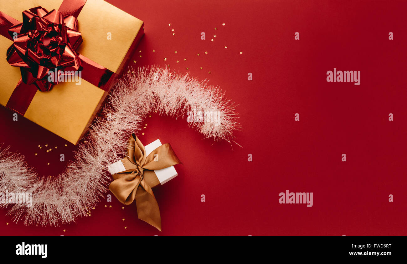 Boîtes cadeaux de différentes tailles avec des étoiles et de la guirlande avec copie espace. Mise à plat des cadeaux et décoration de Noël sur fond rouge. Banque D'Images