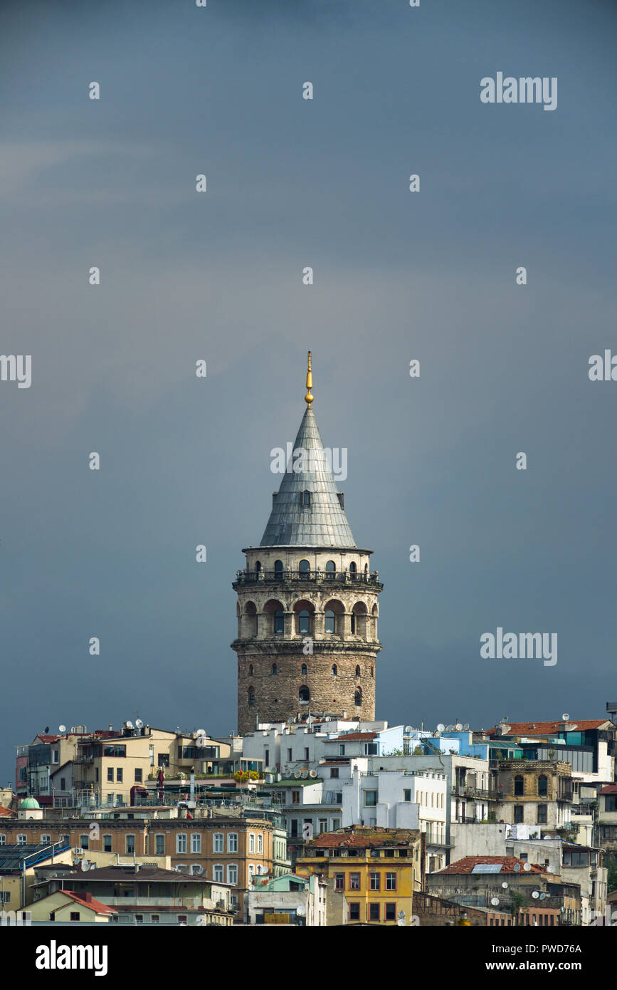 La tour de Galata éclairées par le soleil dominant l'horizon contre des nuages sombres, Istanbul, Turquie Banque D'Images