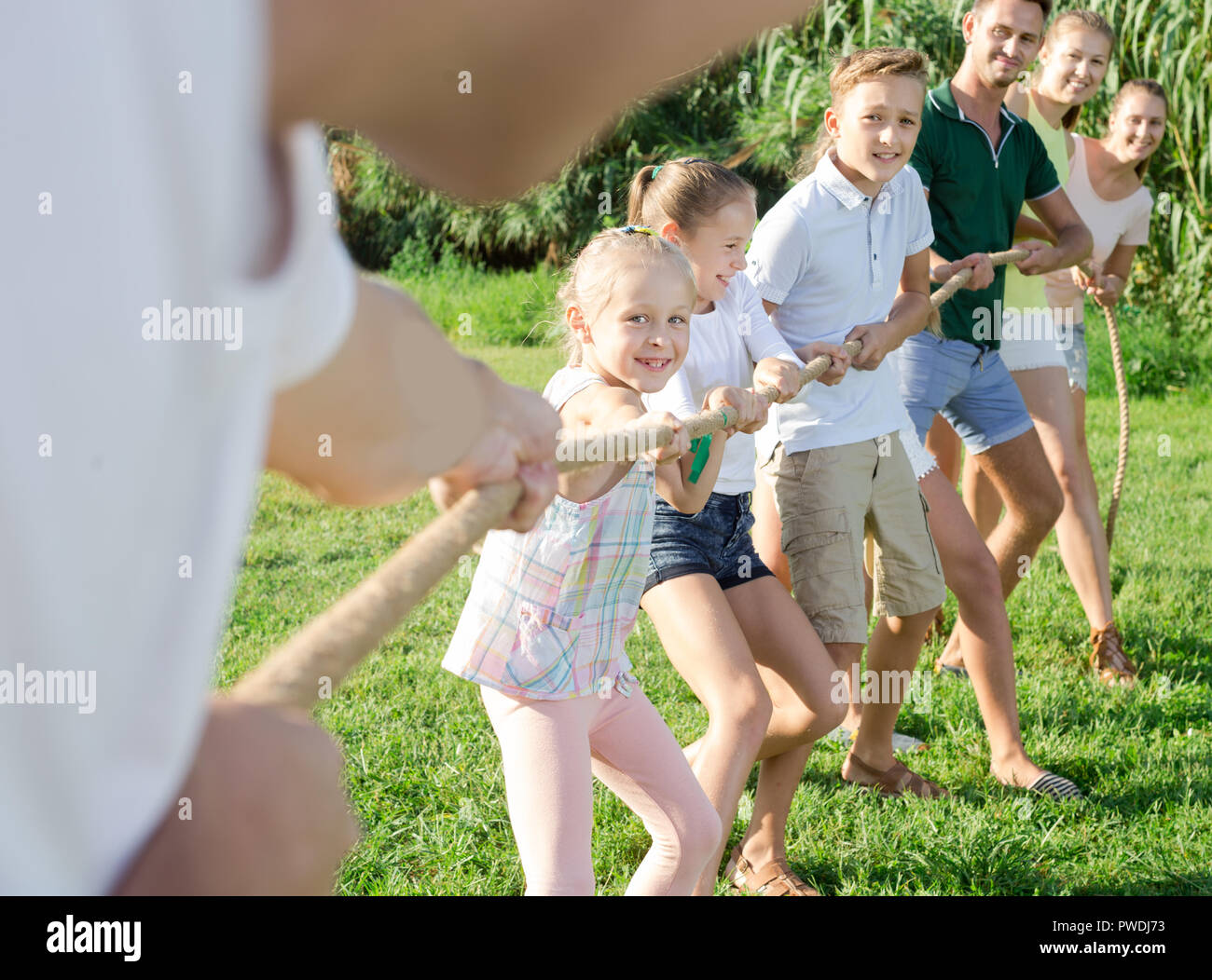 Smiling kids avec les mères et les pères jouer remorqueur de la guerre durant les jeux en plein air aux beaux jours Banque D'Images