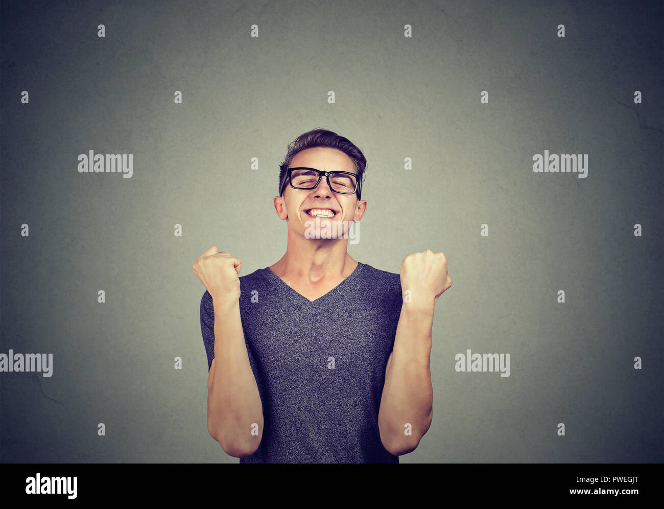 Jeune homme Super excité dans les verres holding poings dans la célébration du succès sur fond gris Banque D'Images