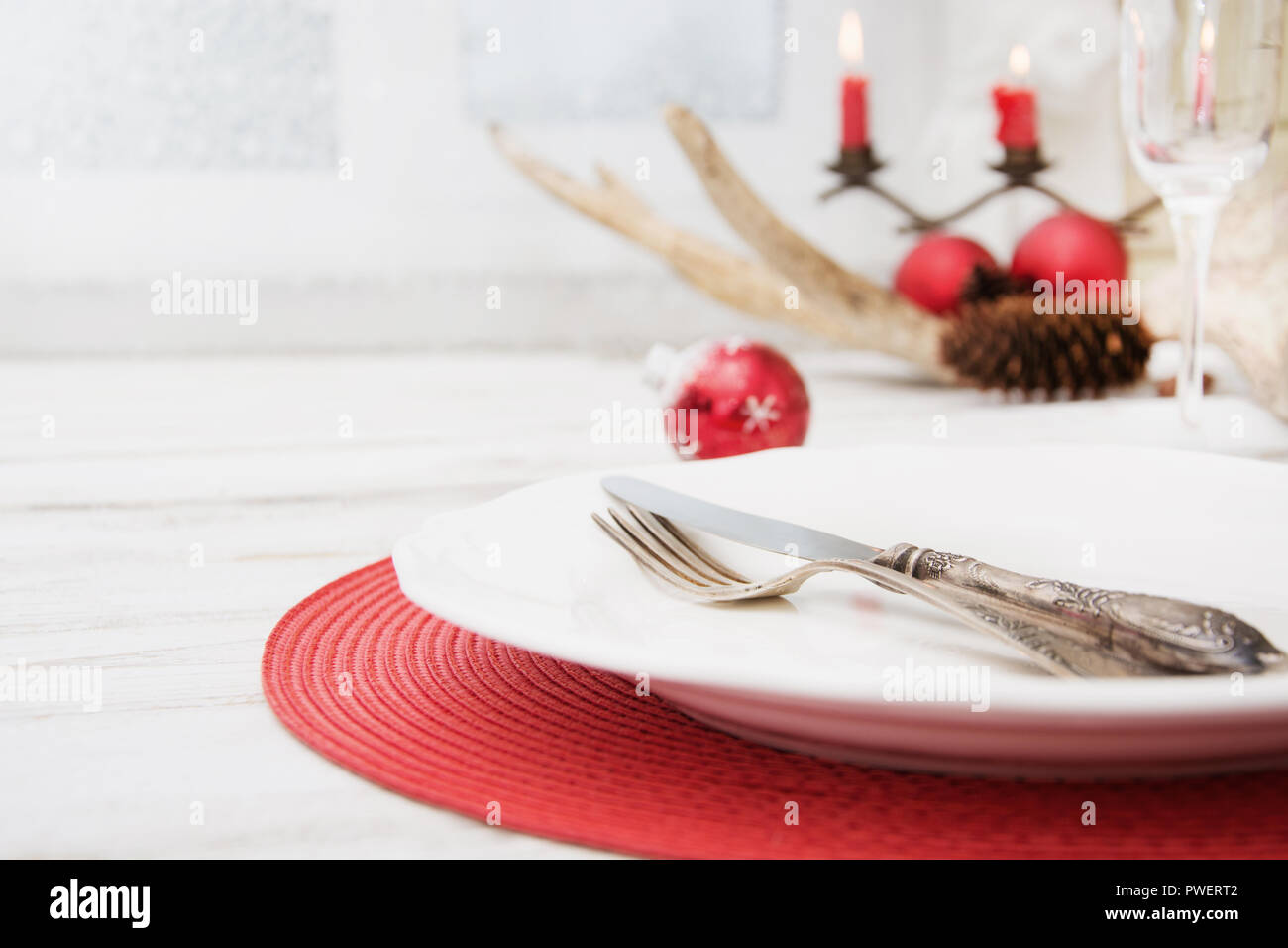 Lieu de Noël blanc avec vaisselle, couverts, vaisselle et décorations rouge sur planche de bois. Chandelier de Noël bougies rouges avec comme décor. Banque D'Images