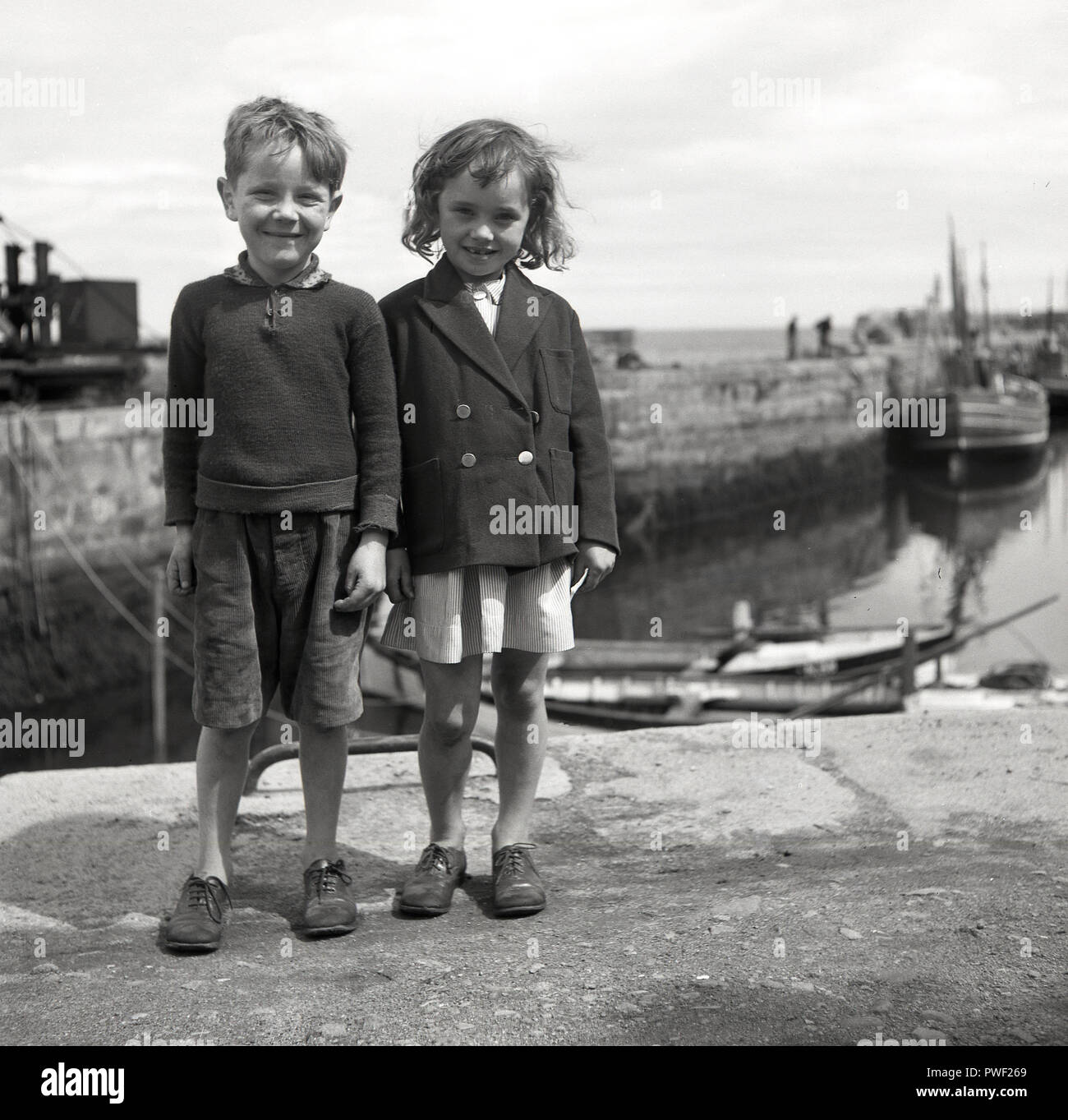 Années 1950, historique, par un petit port de pêche, un jeune garçon et fille irlandaise avec de grands sourires, se tenir ensemble pour une photo, l'Irlande du Nord, Royaume-Uni. Banque D'Images