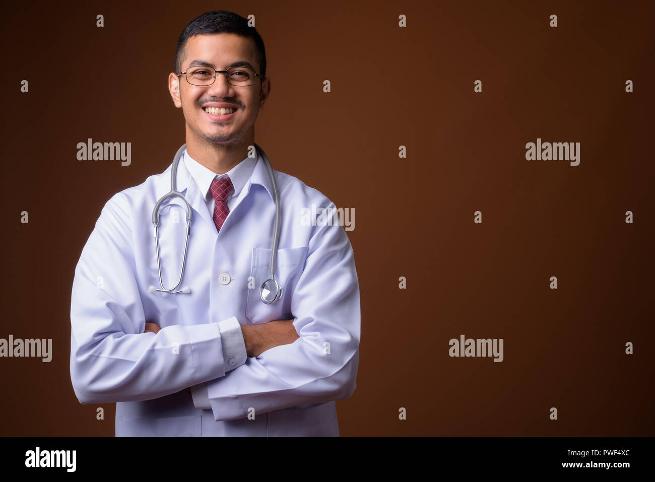 Jeune homme asiatique multi-ethnique médecin contre fond brun Banque D'Images