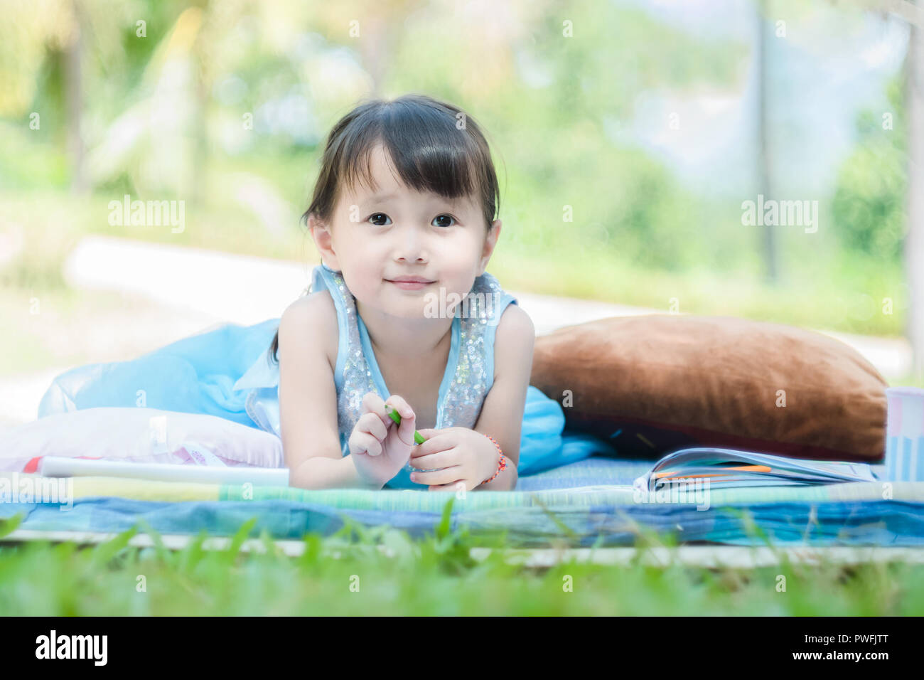 Petite fille couchée avec encombrement livre sur le tapis de parc avec visage heureux quand sa maison de matin en relaxant Banque D'Images