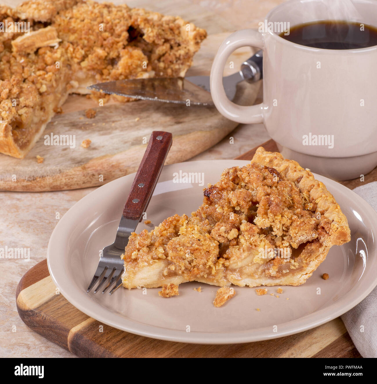 Tranche de tarte aux pommes hollandaise sur une plaque brune avec une tasse de café et des tranches de gâteau sur un plateau en bois en arrière-plan Banque D'Images