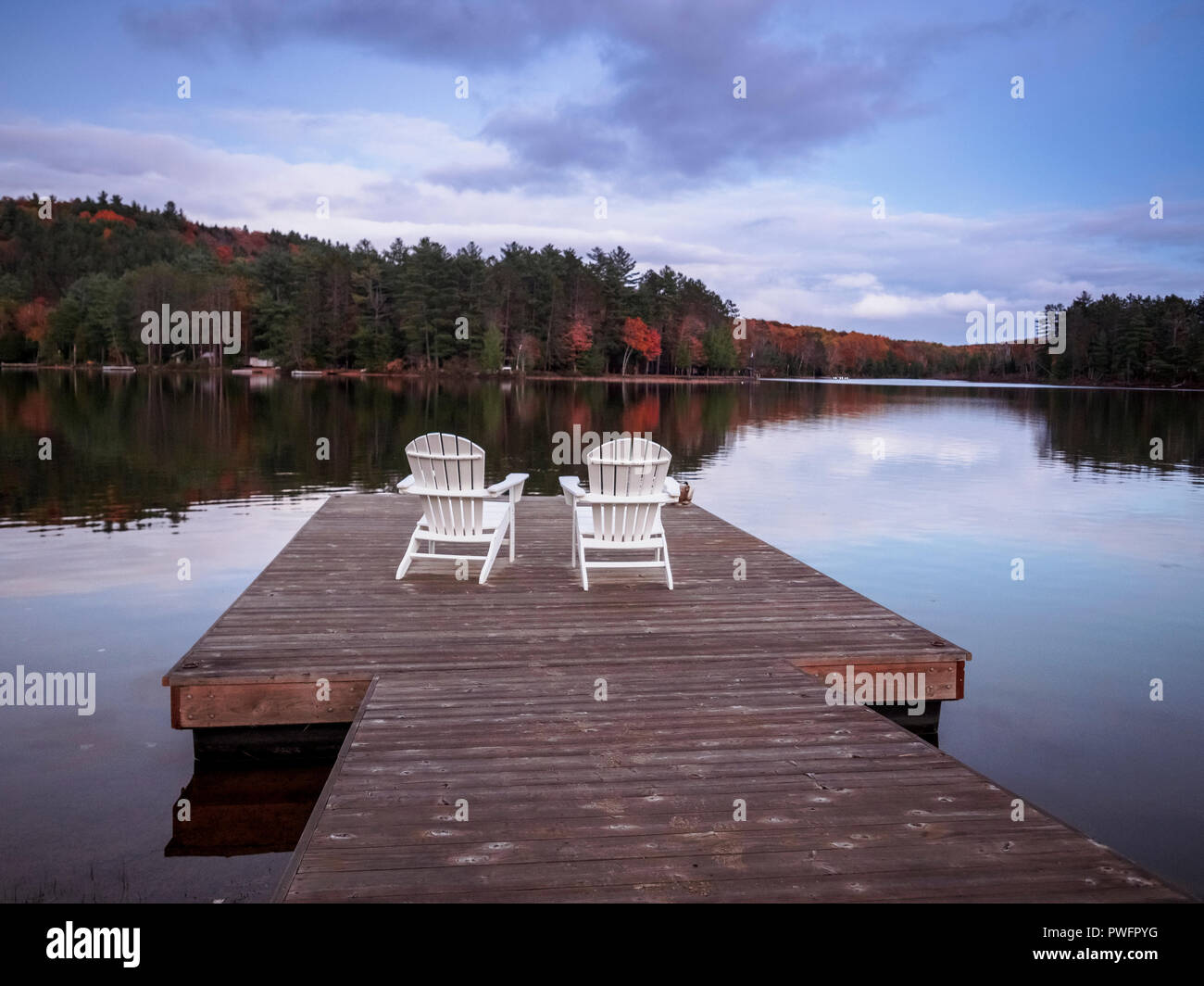 Deux chaises Muskoka en face du lac Ontario, Benoir sur un quai en bois. Le lac calme d'eau donne de superbes reflets. Banque D'Images
