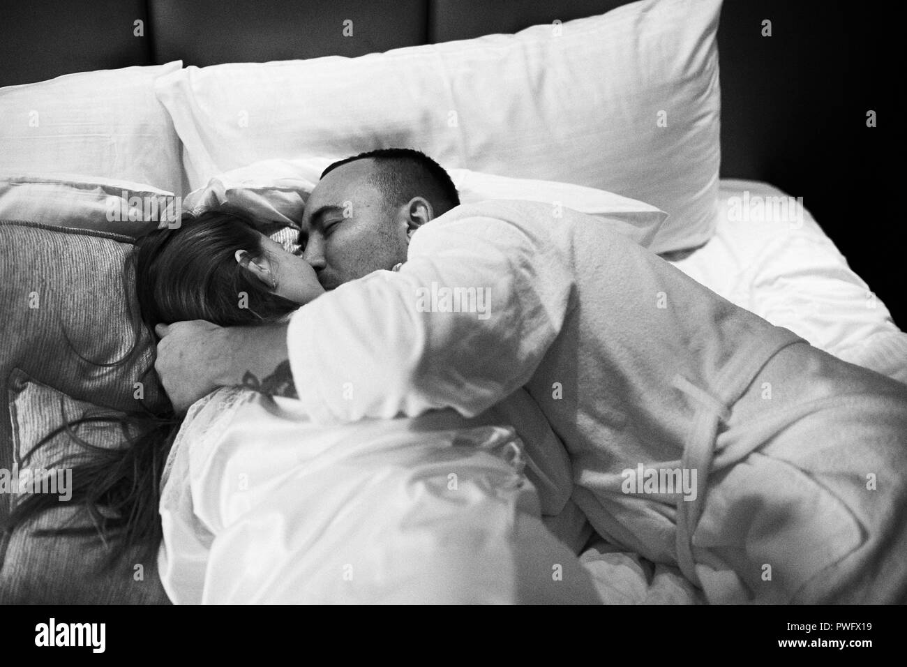 Jeune couple romantique et s'embrasser dans le lit. Jolie fille brune et l'homme. Photo en noir et blanc. Banque D'Images