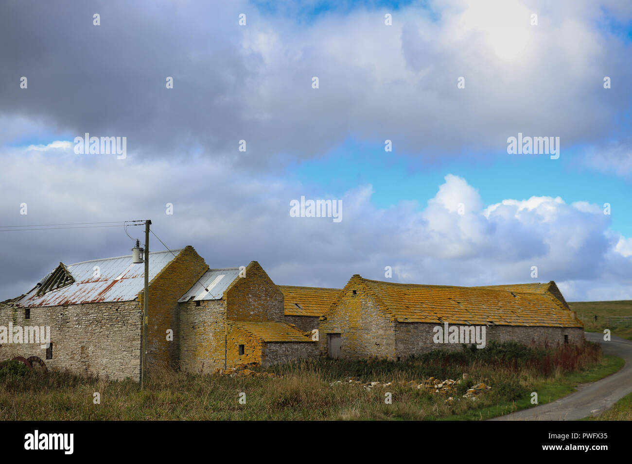 Vieilles granges en pierre avec des toits couverts de lichen jaune, sous un ciel bleu avec des nuages blancs qui ondulent, herbe verte, sur l'île de Rousay, Orkney, Scotland Banque D'Images