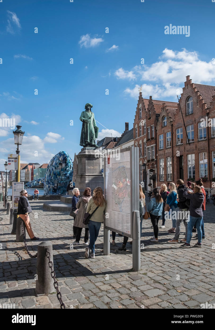 Un groupe de jeunes femmes touristes écouter un guide à la place de Jan Van Eyck, sous une statue de la peintre flamand, Bruges, Flandre occidentale, Belgique Banque D'Images