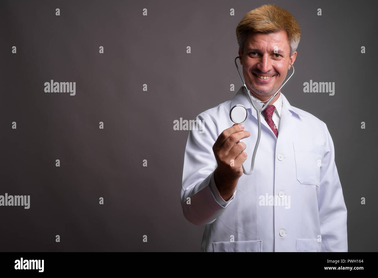 Médecin de l'homme aux cheveux blonds en utilisant stéthoscope contre zone grise Banque D'Images