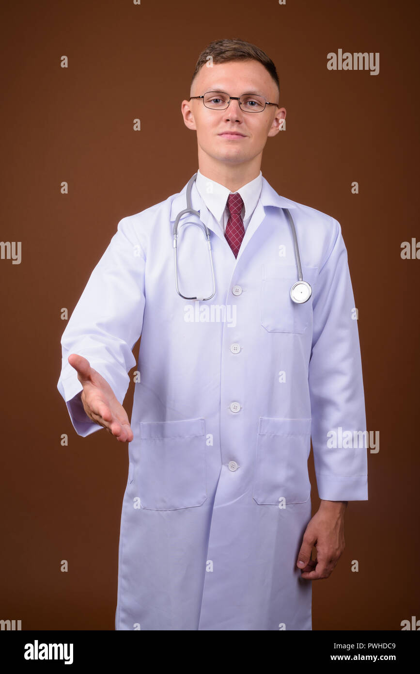 Jeune homme médecin portant des lunettes contre fond brun Banque D'Images