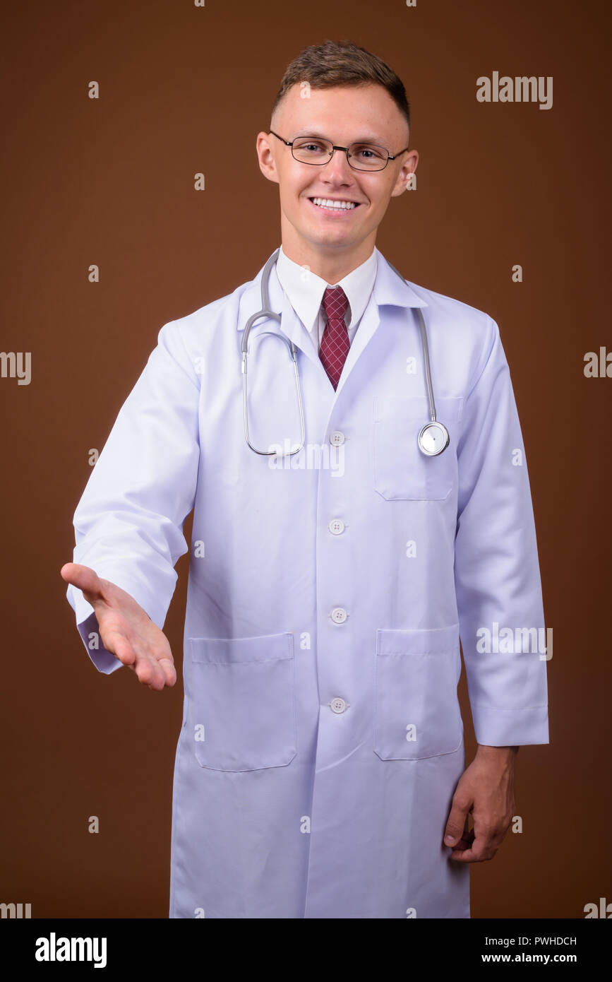 Jeune homme médecin portant des lunettes contre fond brun Banque D'Images