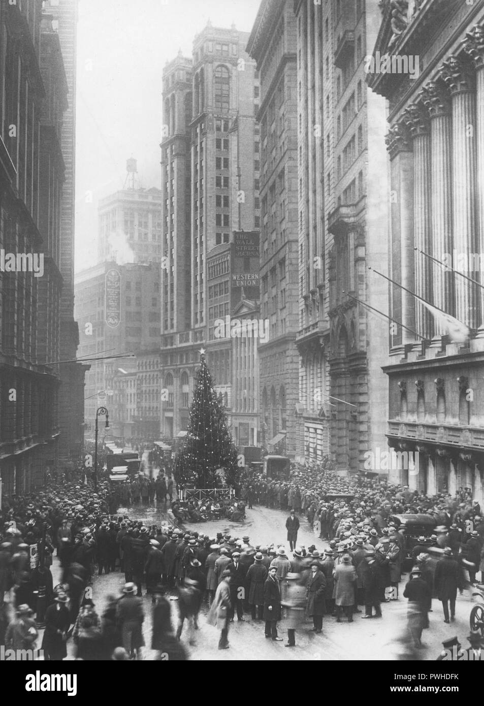 Noël dans les années 1920. Un grand arbre de Noël est debout au milieu de Wall Street à New York. Les gens se sont réunis autour de lui pour écouter la musique de la bande qui joue assis sous l'arbre. Sur la droite du bâtiment abritant la Bourse le 11 Wall street. 26 décembre 1925. Banque D'Images
