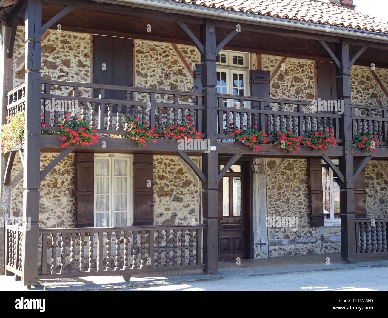 Vieille façade en pierre typique avec des pots de fleurs rouge vif sur le balcon dans le sud-ouest de la France l Banque D'Images