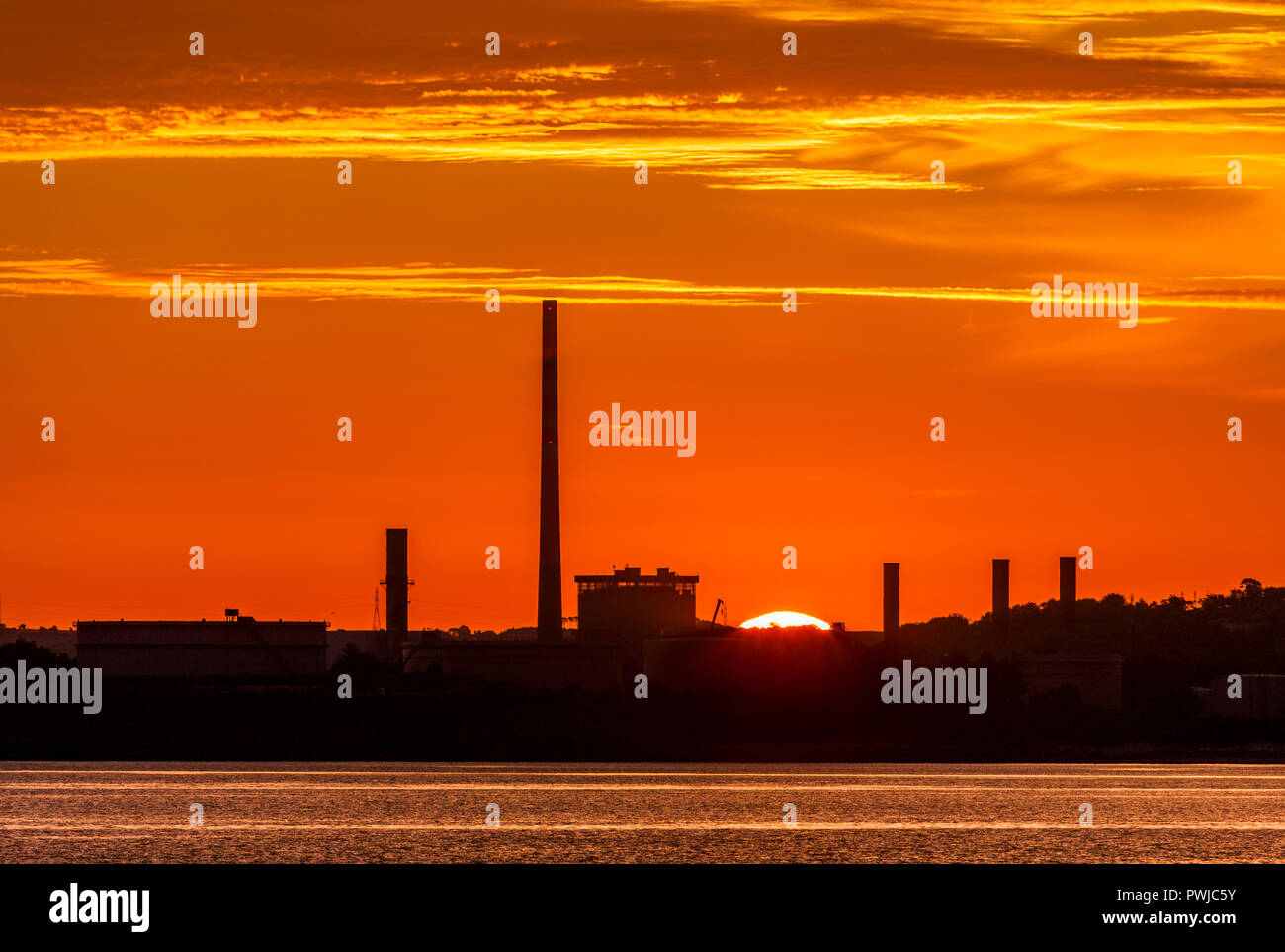 Whitegate, Cork, Irlande, le 18 juillet 2017. Raffinerie de pétrole et la Whitegate ESB à Aghada silhouetté par le soleil levant à Cork harbou Banque D'Images