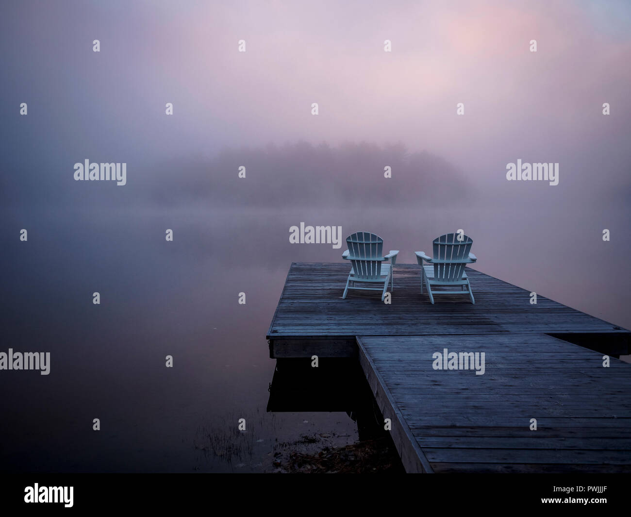 Deux chaises Muskoka en face du lac Ontario, Benoir sur un quai en bois. Vraiment un jour brumeux sur la lumière tôt le matin avec la brume rose et orange en raison de l'aube Banque D'Images