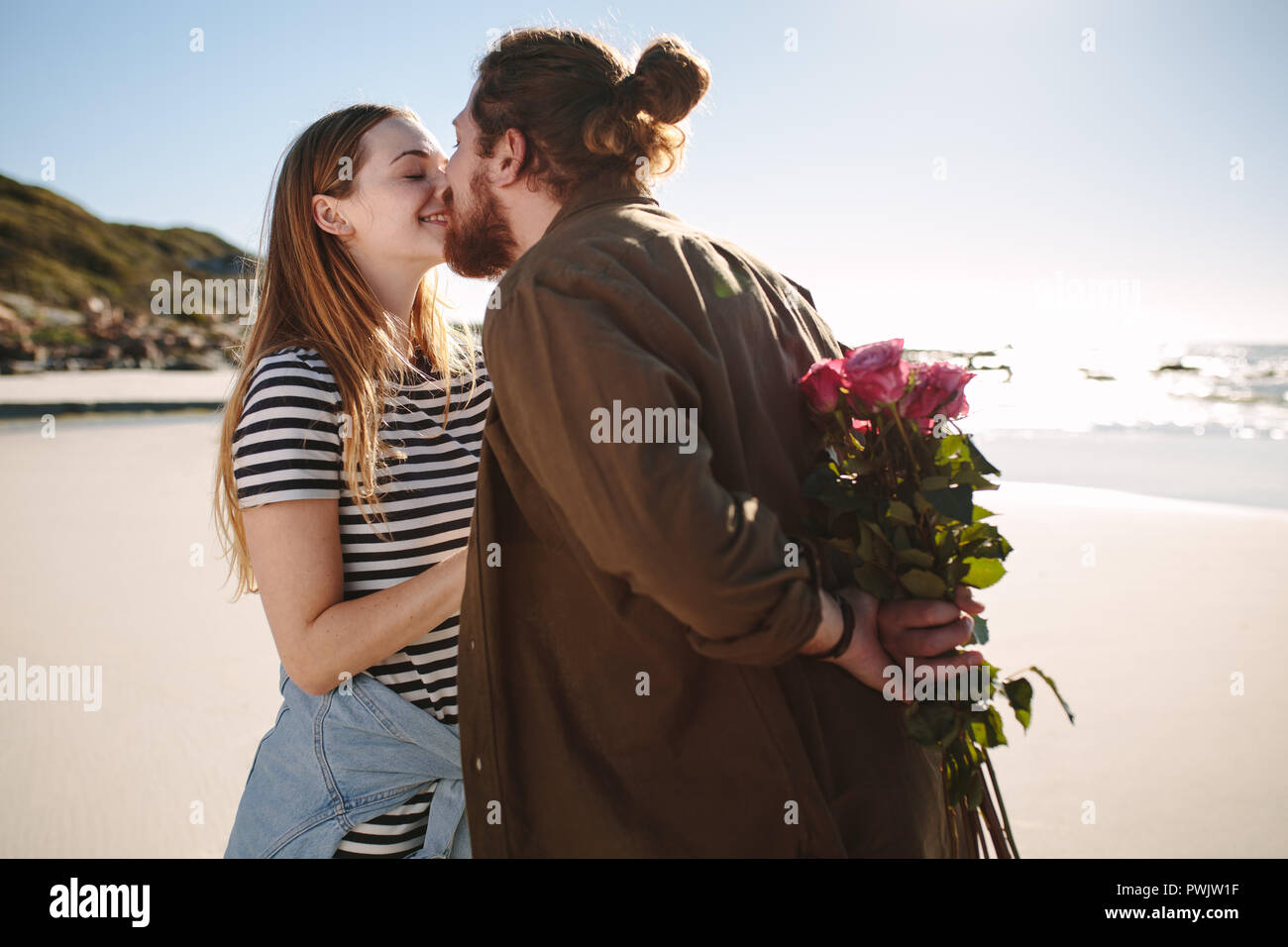 Petit ami holding surprise bouquet de fleurs pour l'amie sur la plage. Couple romantique sur une date romantique à la plage. Banque D'Images